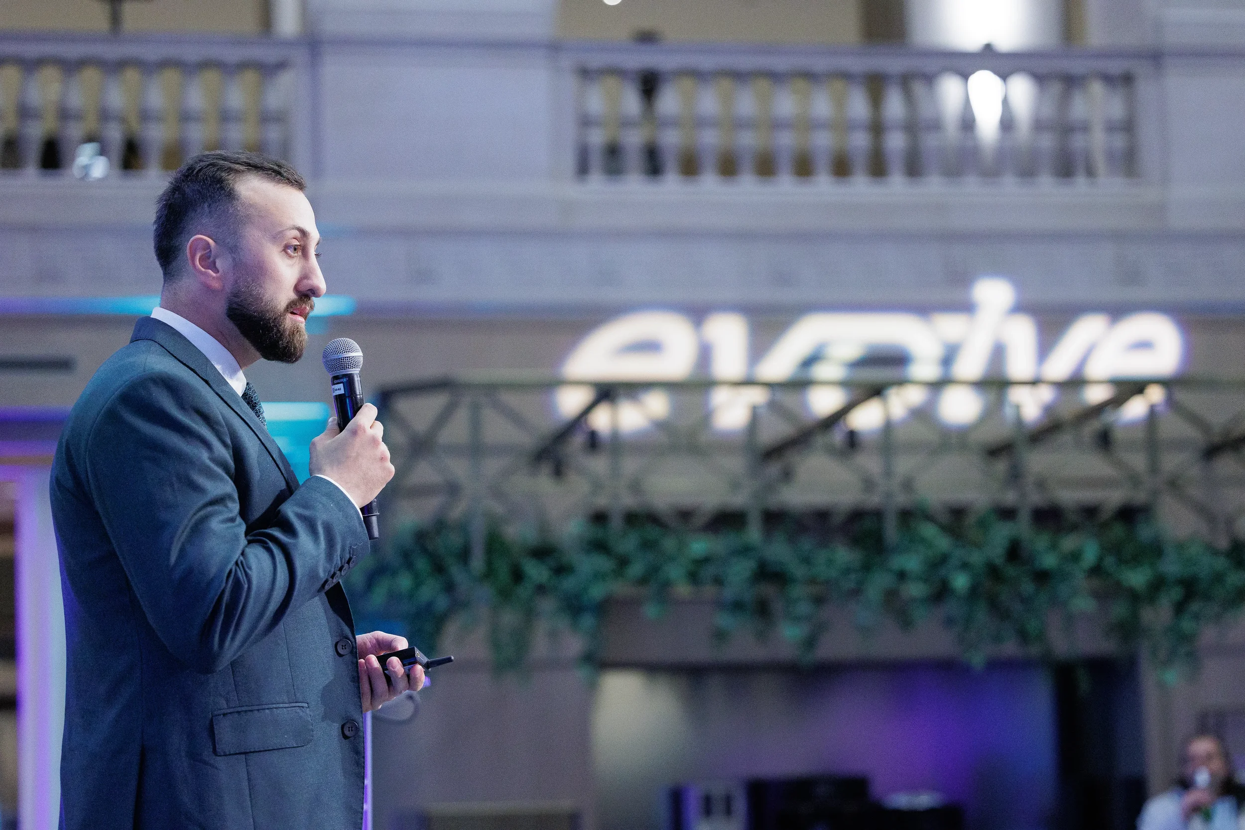 Speaker holds microphone on stage with illuminated brand sign in atrium backdrop at Orlando corporate event