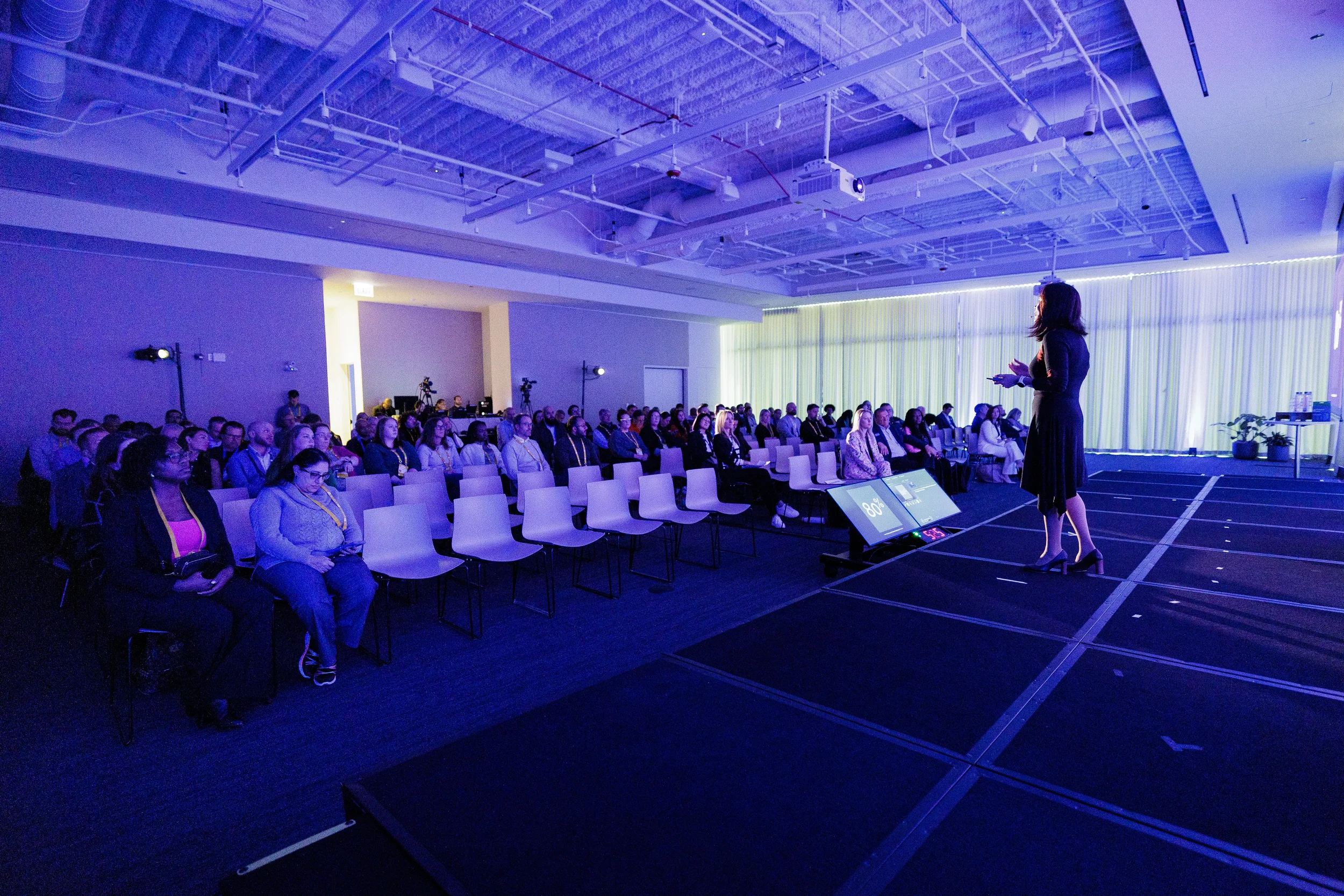 Presenter addresses seated audience during session in purple-lit room at Orlando corporate conference