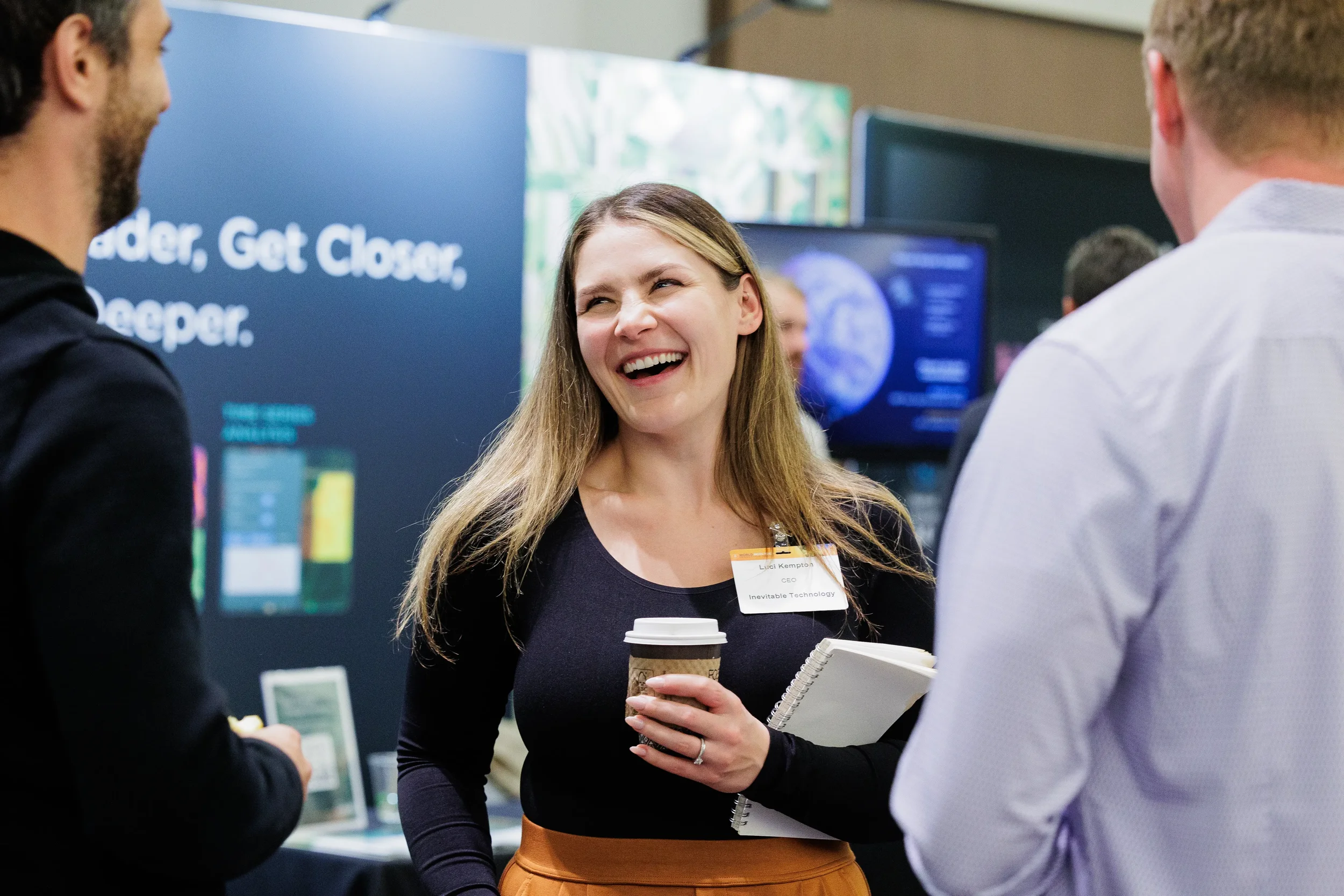Smiling badged attendee with coffee and notebook laughs during networking at Chicago industry conference