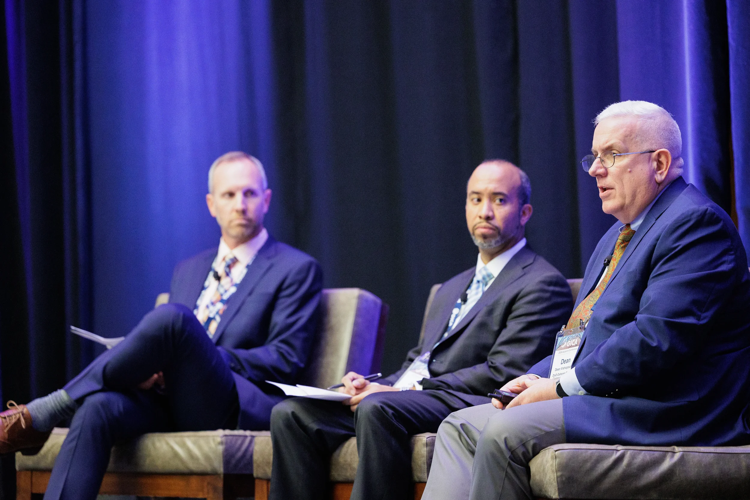 Three businessmen in suits sit on a stage before a deep blue curtain during a panel discussion in Orlando.