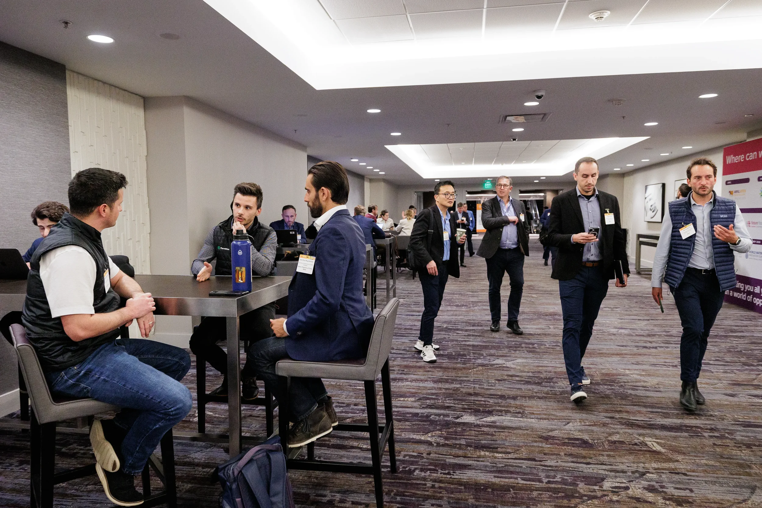 Badged attendees network at high-top tables and walk through hotel hallway at Orlando corporate conference