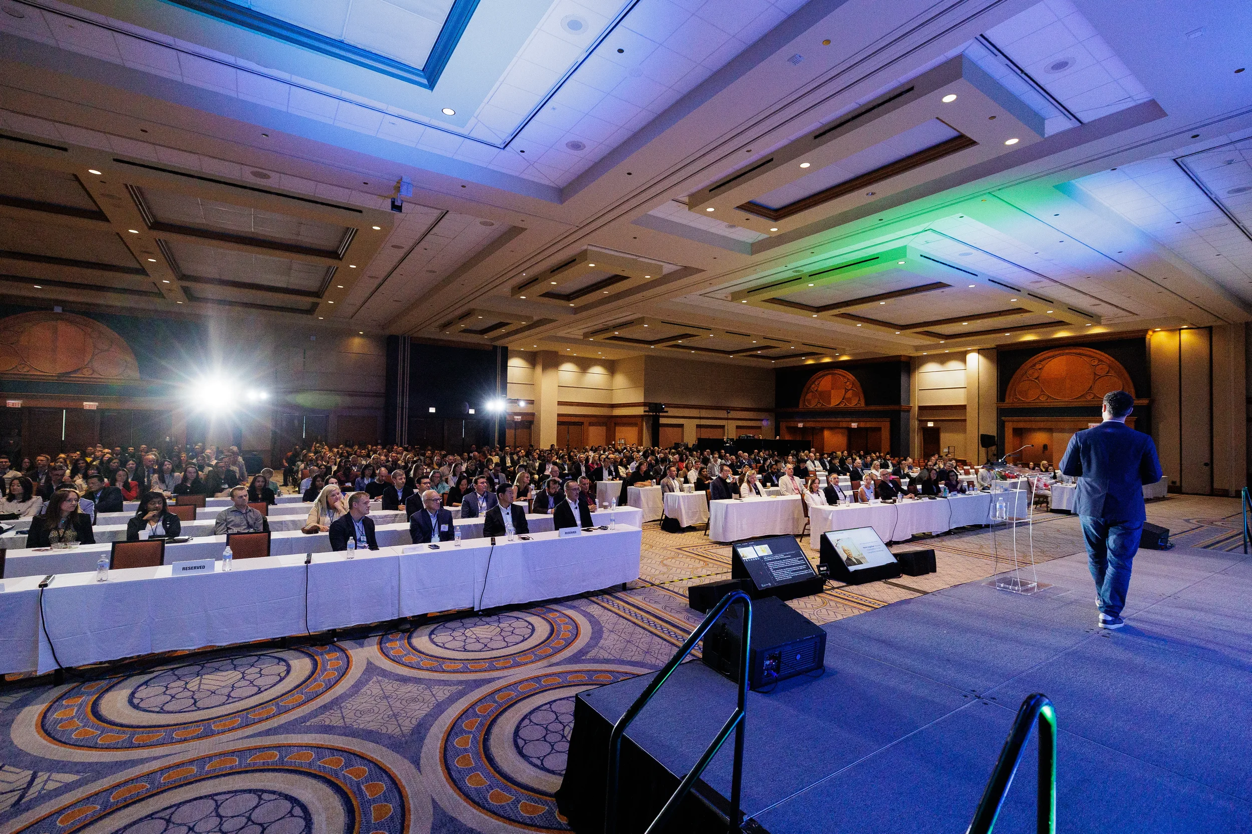 Wide view of speaker addressing seated audience in ballroom at Orlando corporate conference