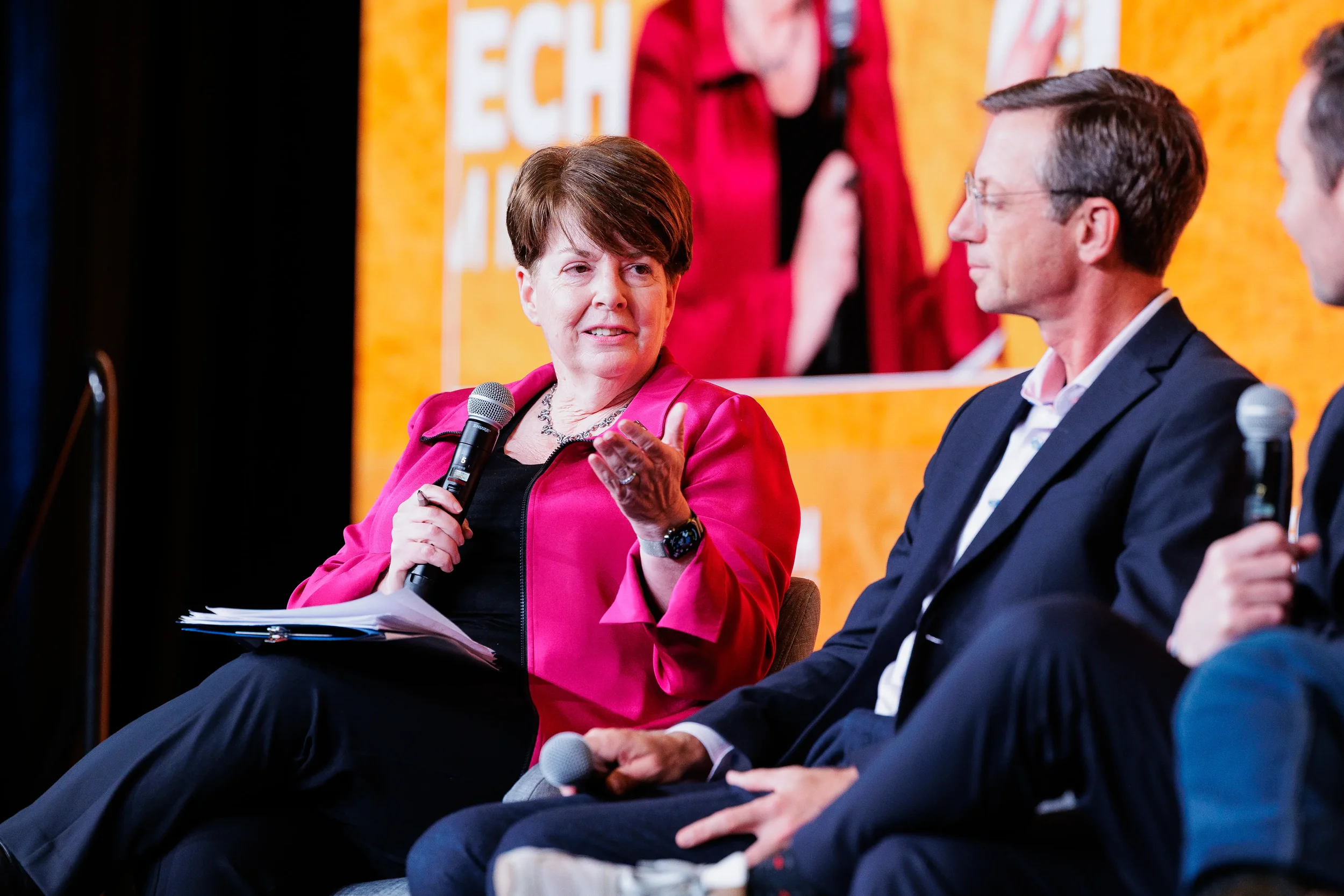 Female panelist in pink jacket holds microphone and gestures on stage at Chicago industry conference