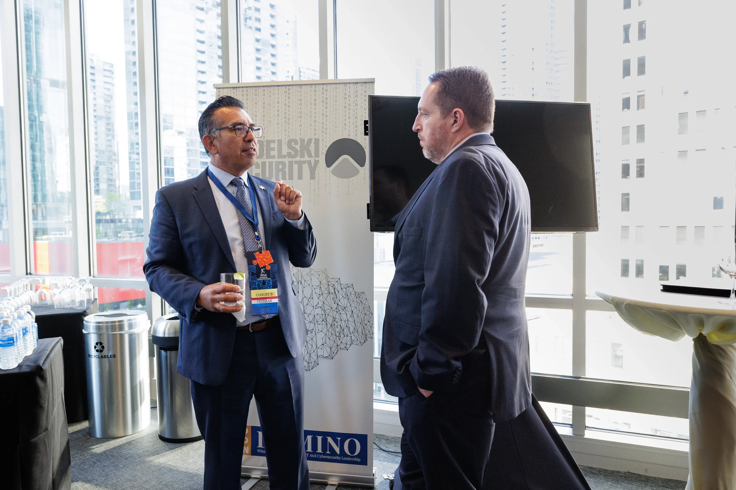 Two male attendees with lanyards converse near branded banner with city skyline at Orlando corporate event