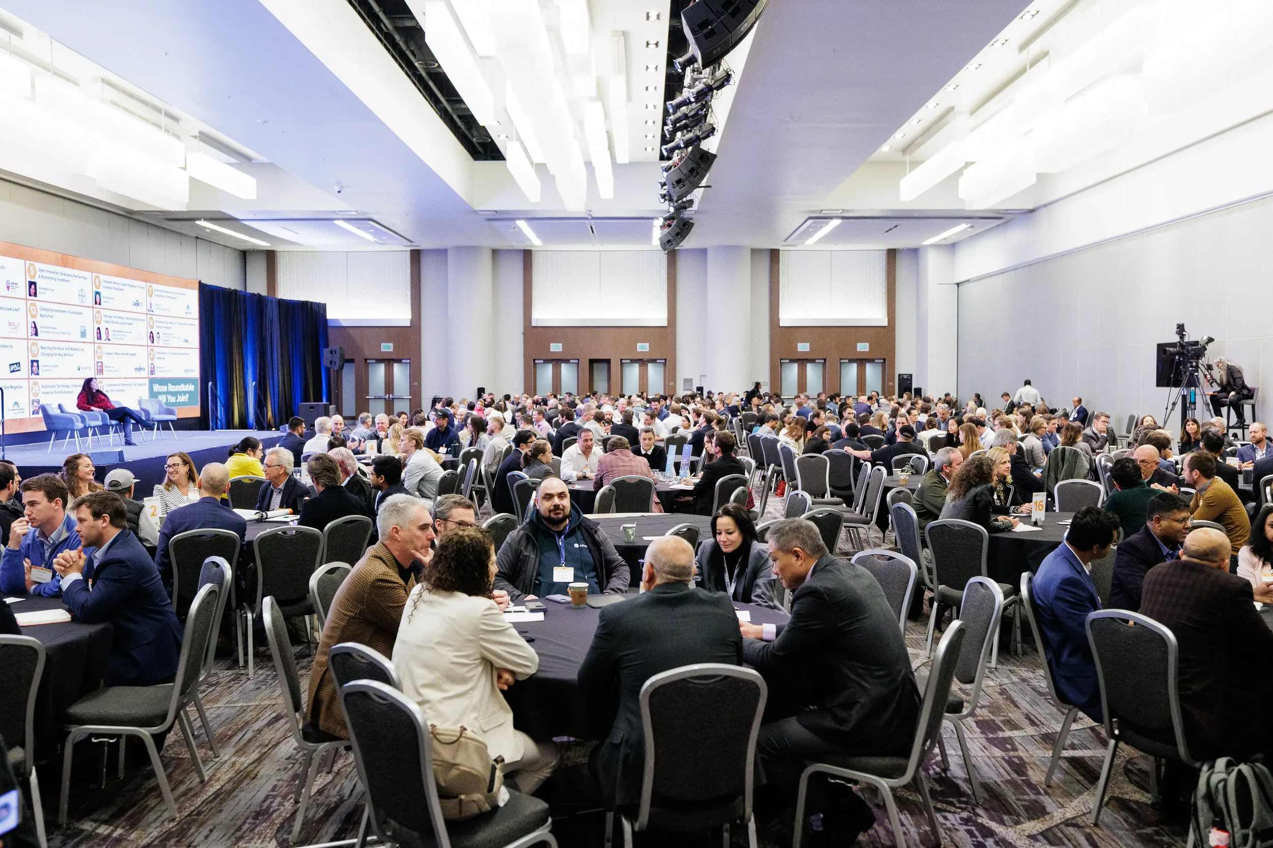 Wide view of attendees at roundtable discussions with stage panel at Orlando industry conference