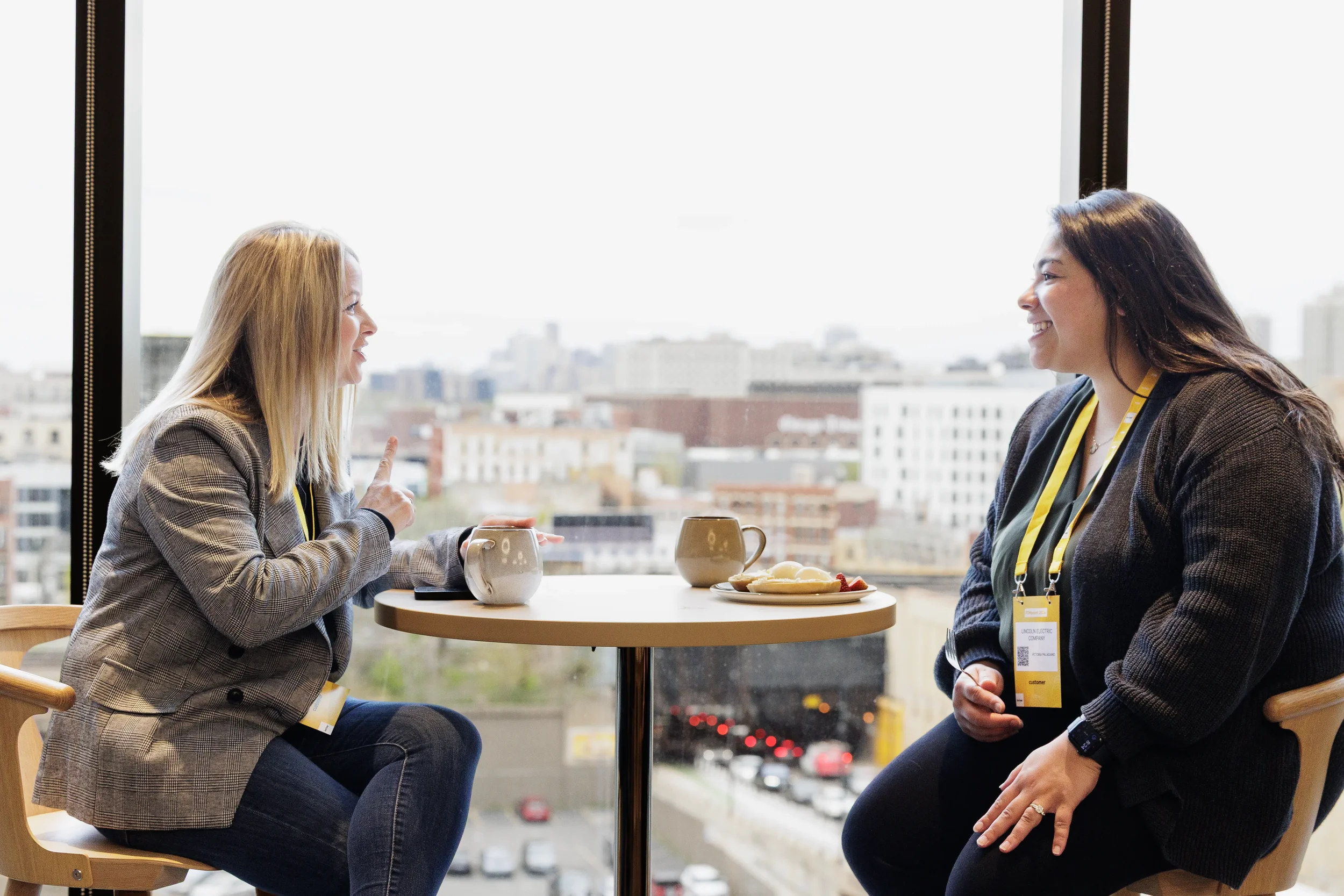 Two attendees talk over coffee at window table with city view at Chicago corporate conference