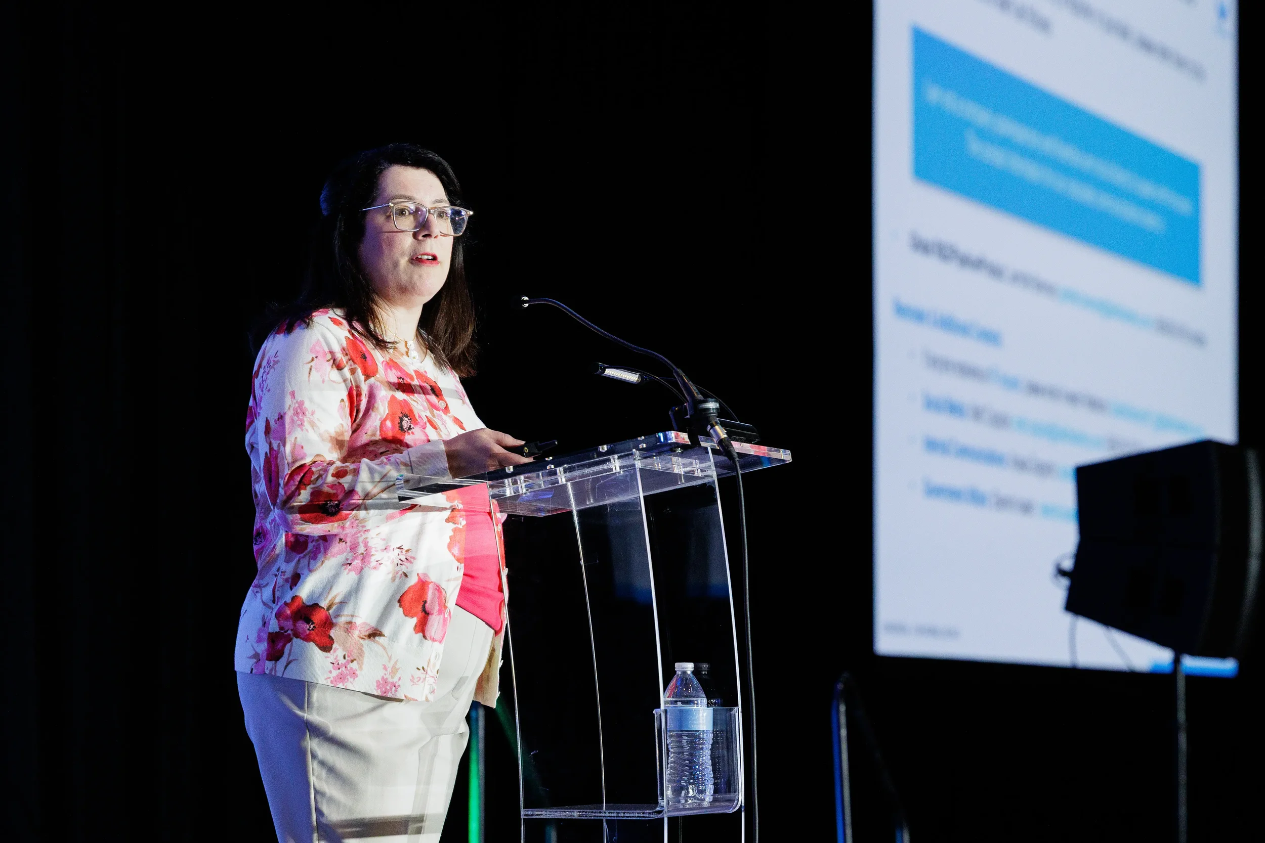 Speaker addresses audience from podium with presentation screen at Orlando corporate event