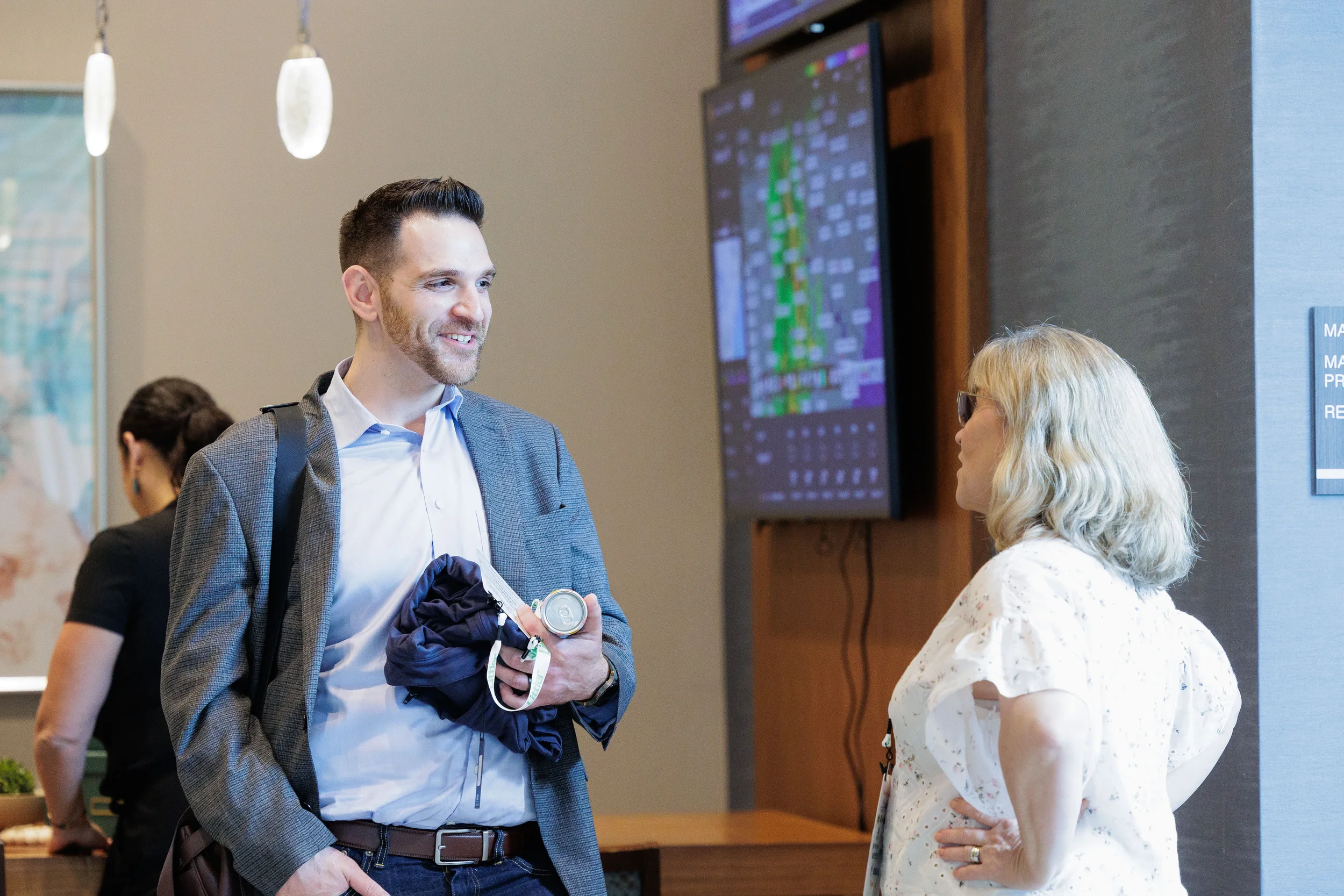 Two attendees smile and chat near digital display screen during Orlando corporate conference networking