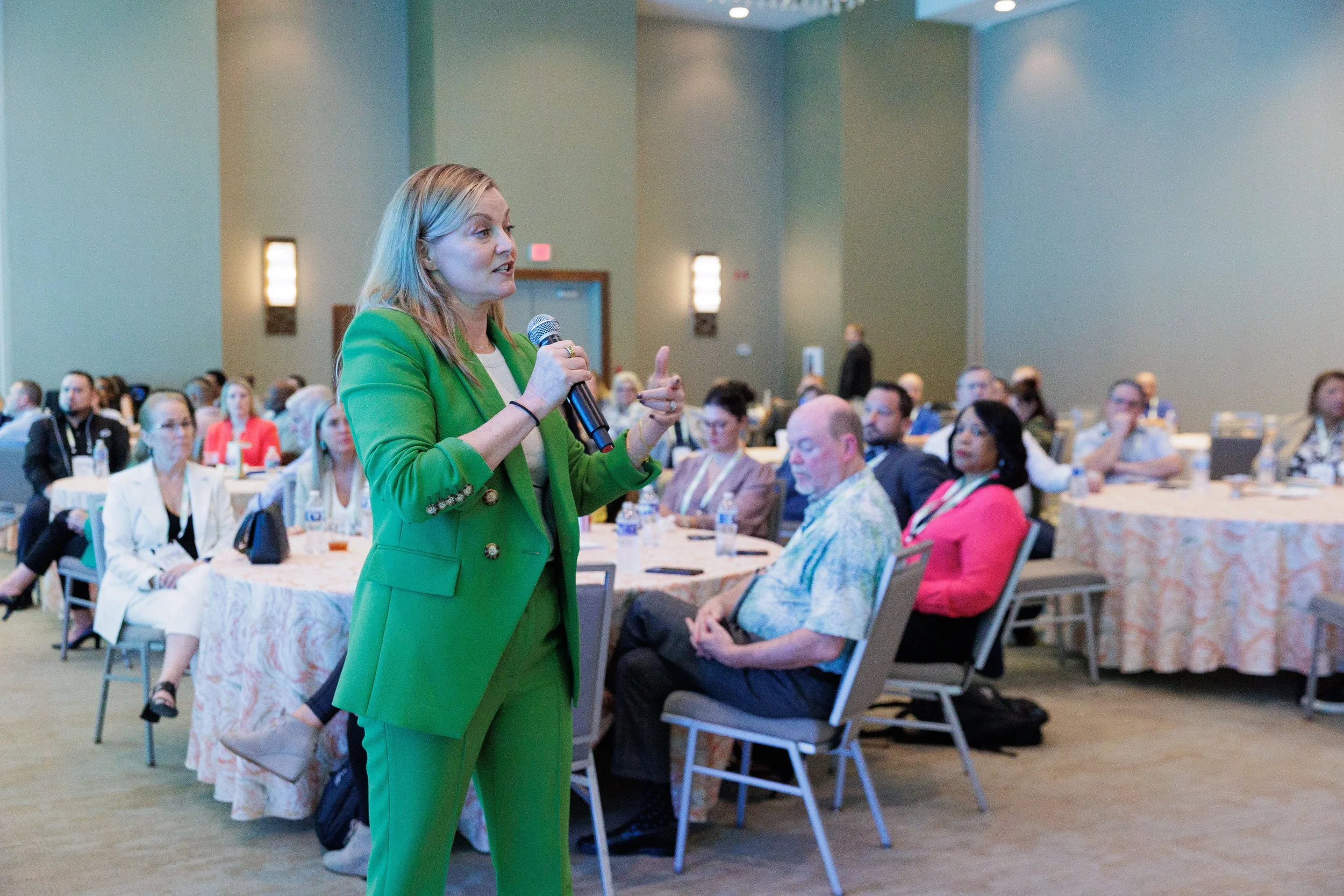 Speaker in green suit holds microphone and gestures while addressing seated attendees at Chicago corporate event