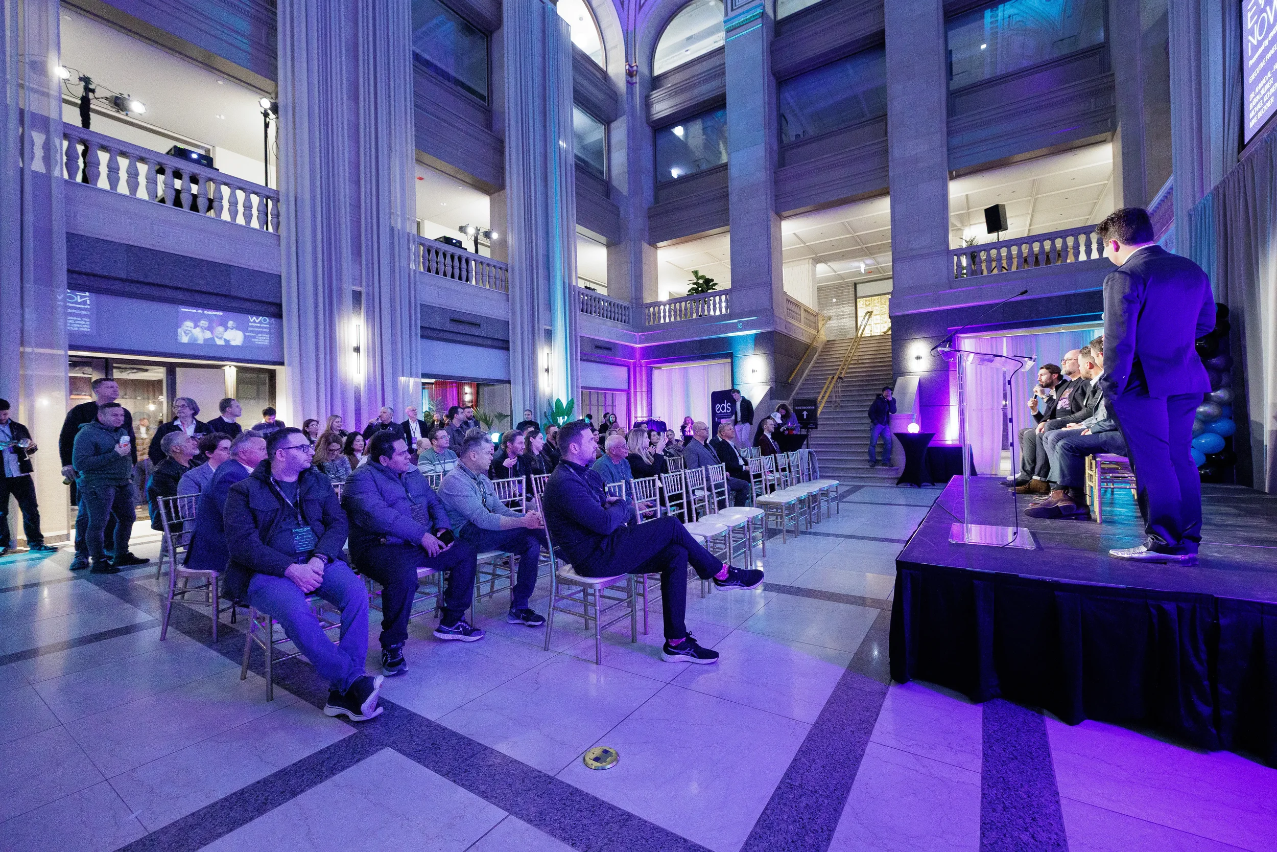 Speaker presents from podium to seated audience in multi-story atrium at Orlando corporate event