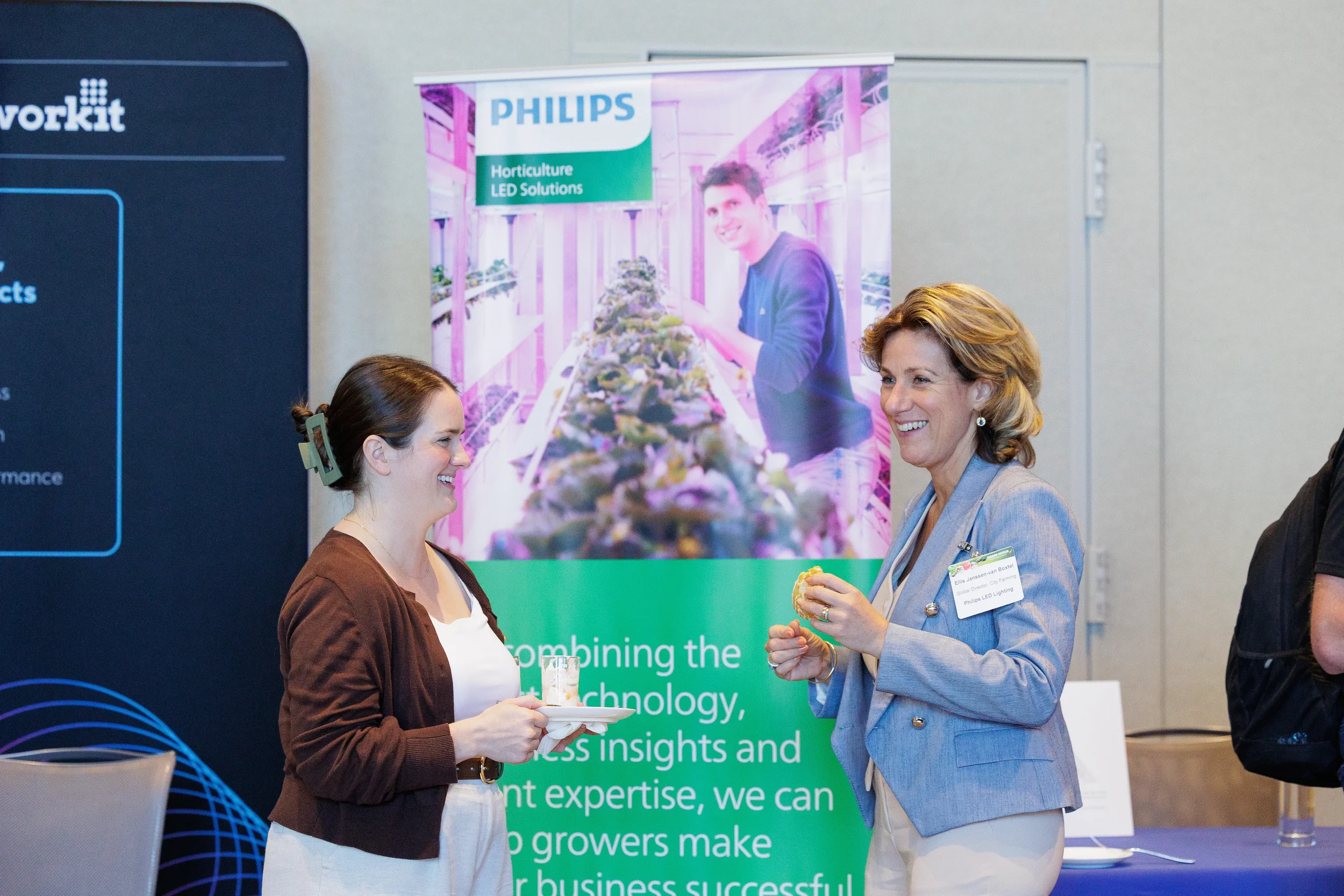 Two attendees share a laugh in conversation beside sponsor booth banner at Orlando industry conference expo floor