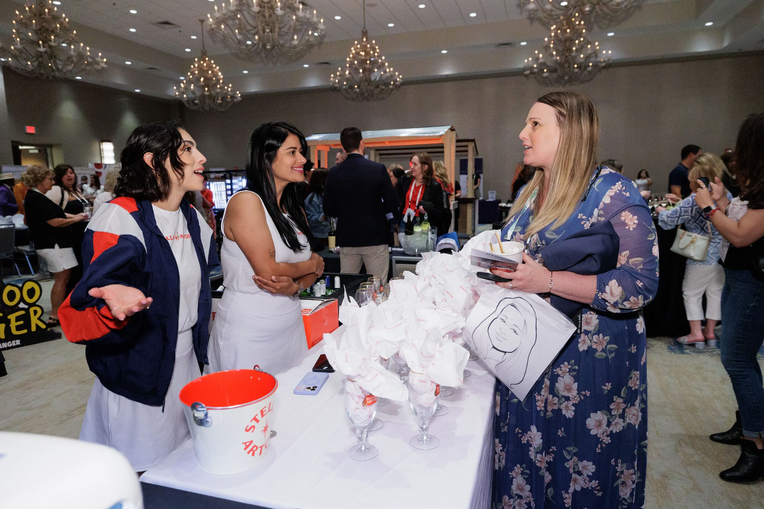 Two booth staff chat with attendee beside wrapped glassware display at Orlando industry conference expo