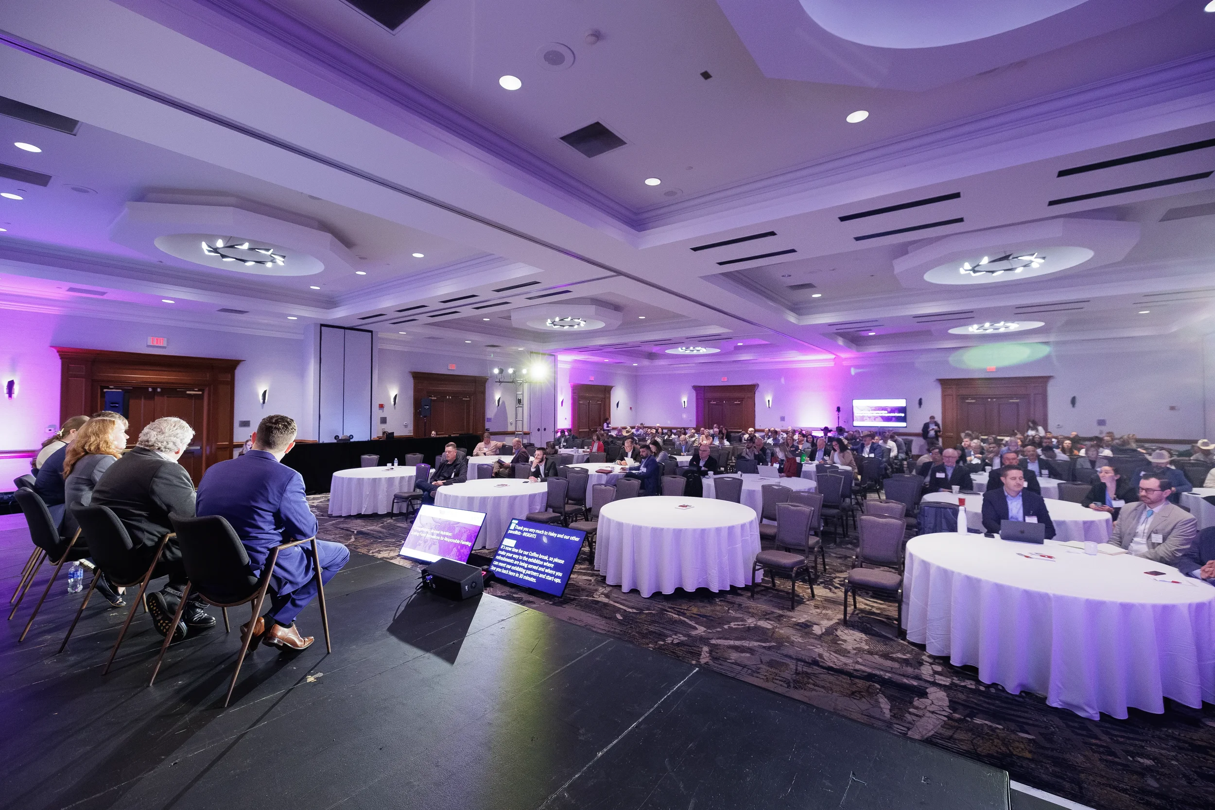 Wide view of seated audience at round tables during session at Orlando corporate conference