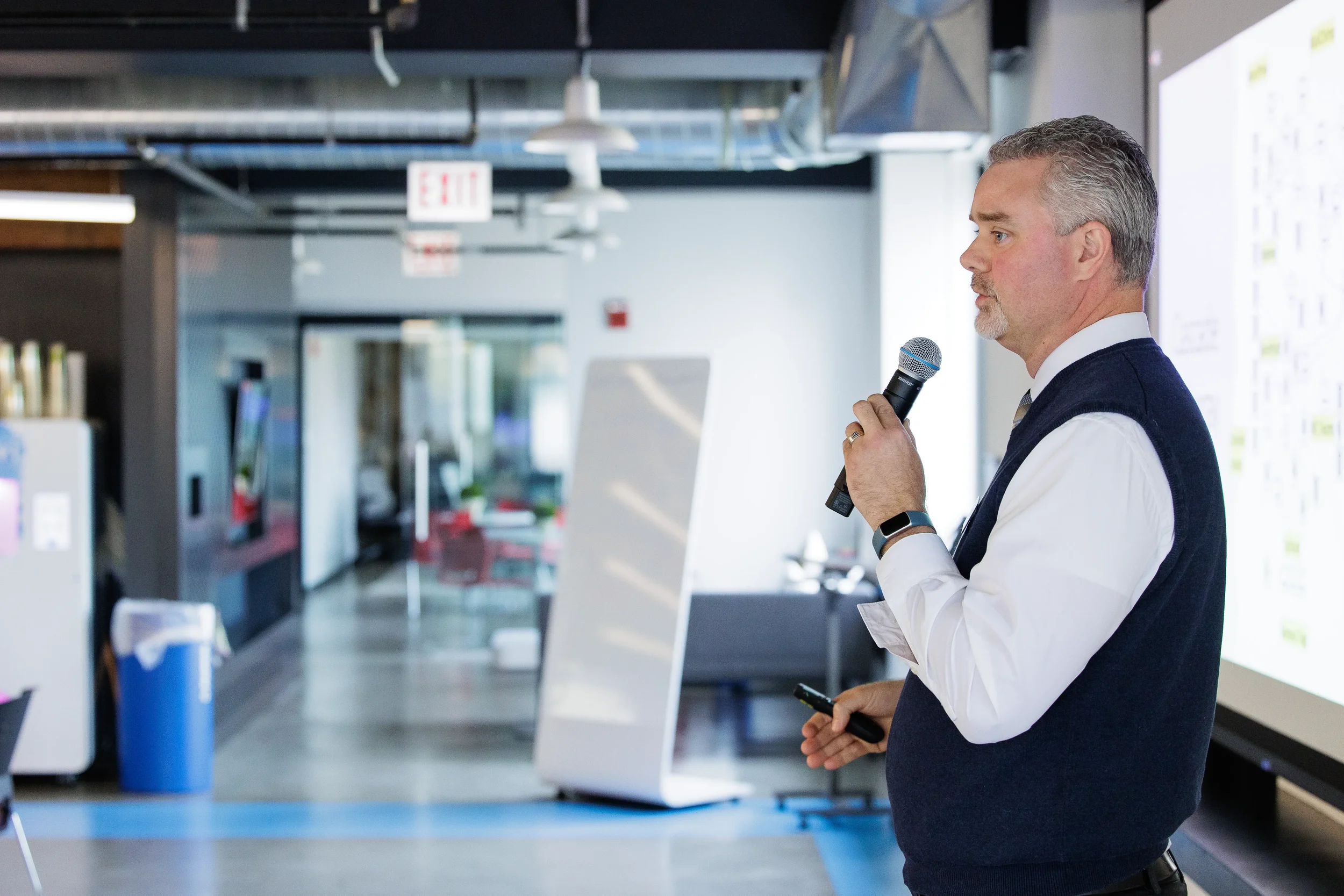 Male speaker holds microphone beside large projection screen at Chicago corporate event