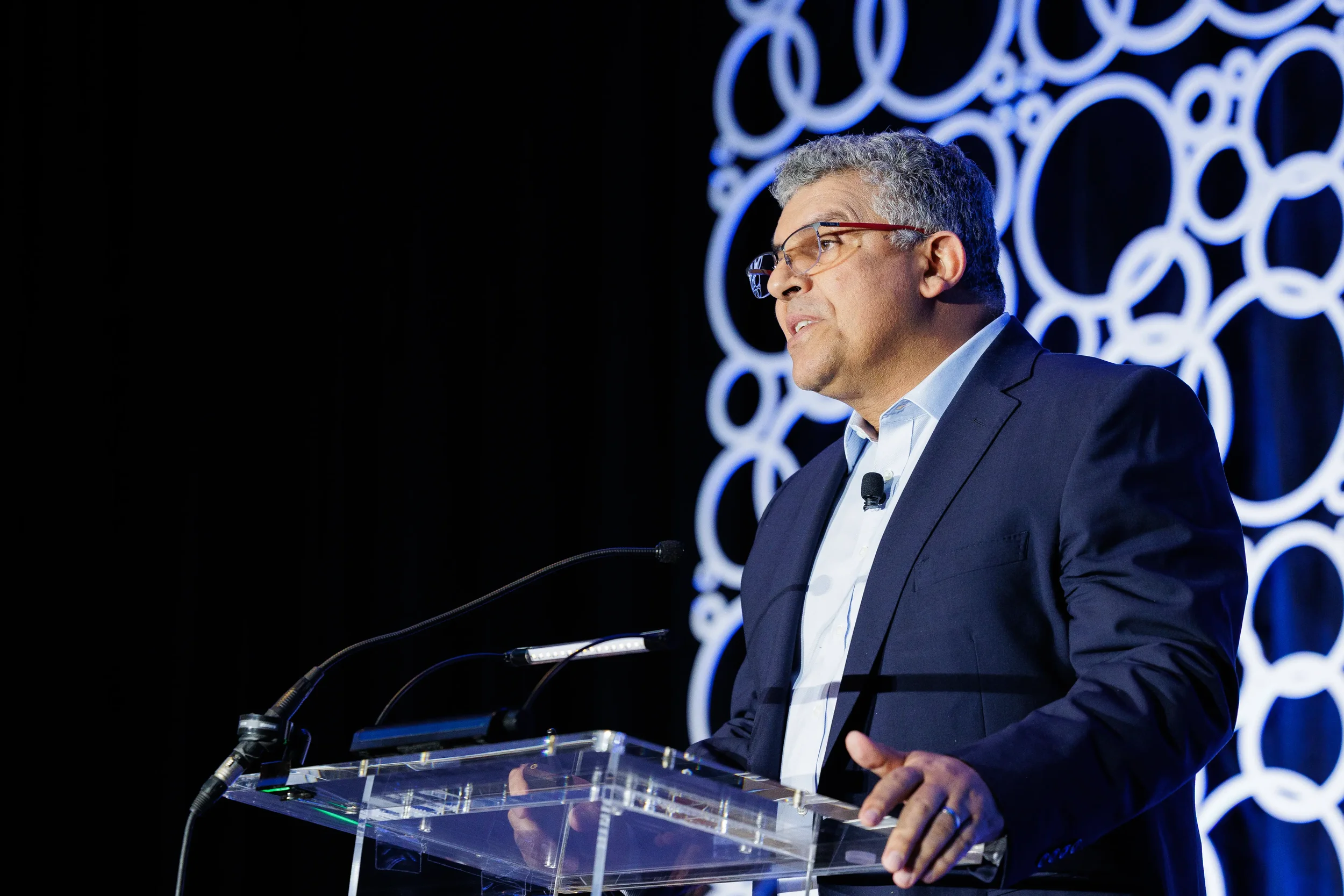 Keynote speaker with red-framed glasses talks at acrylic lectern during Orlando corporate event