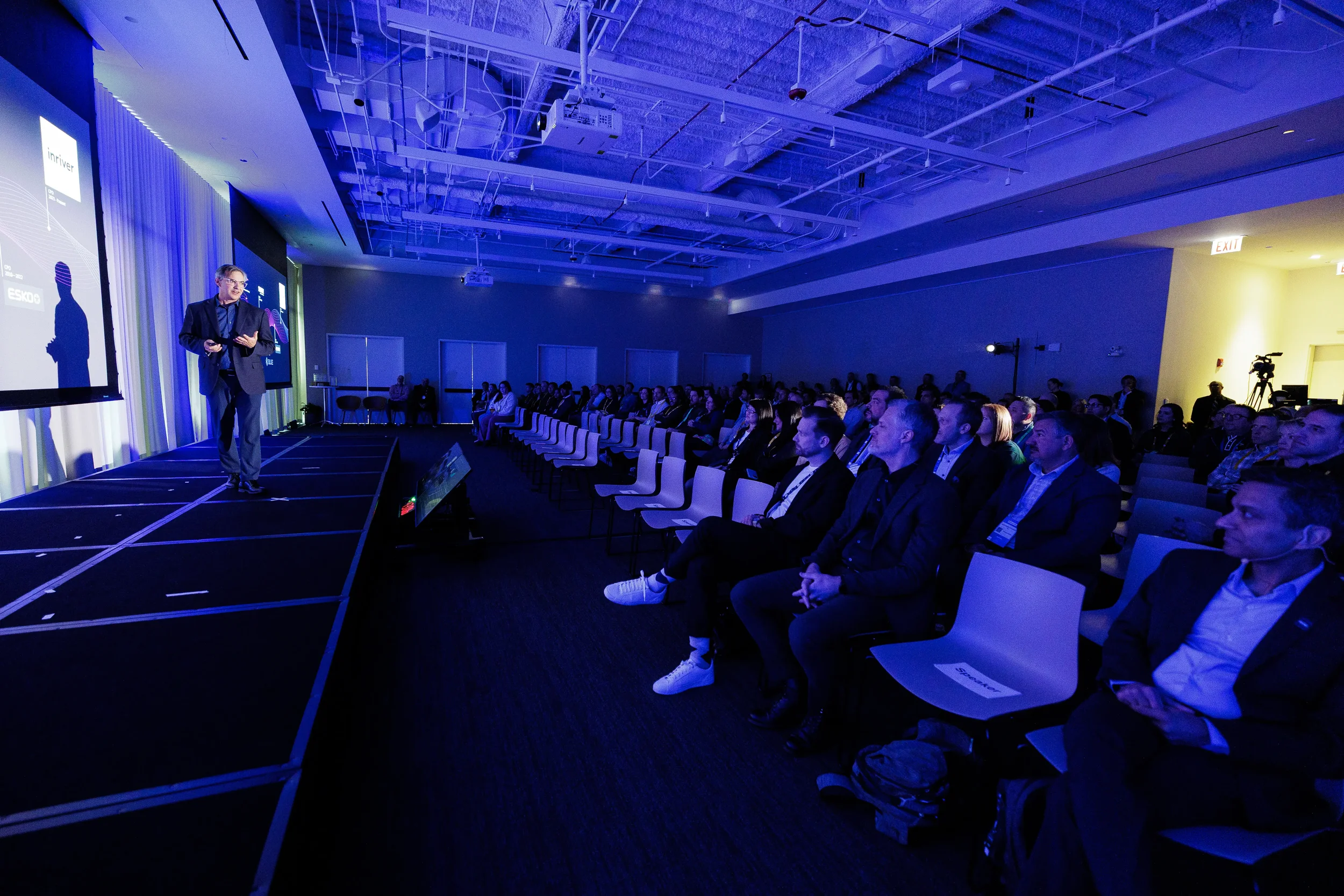 Speaker presents to seated audience in blue-lit room at Chicago industry conference
