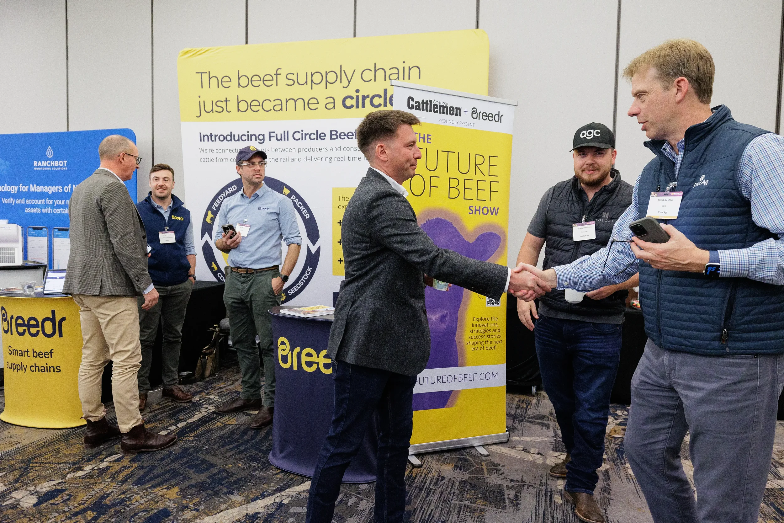 Attendees shake hands at exhibitor booth on expo floor during Orlando corporate conference
