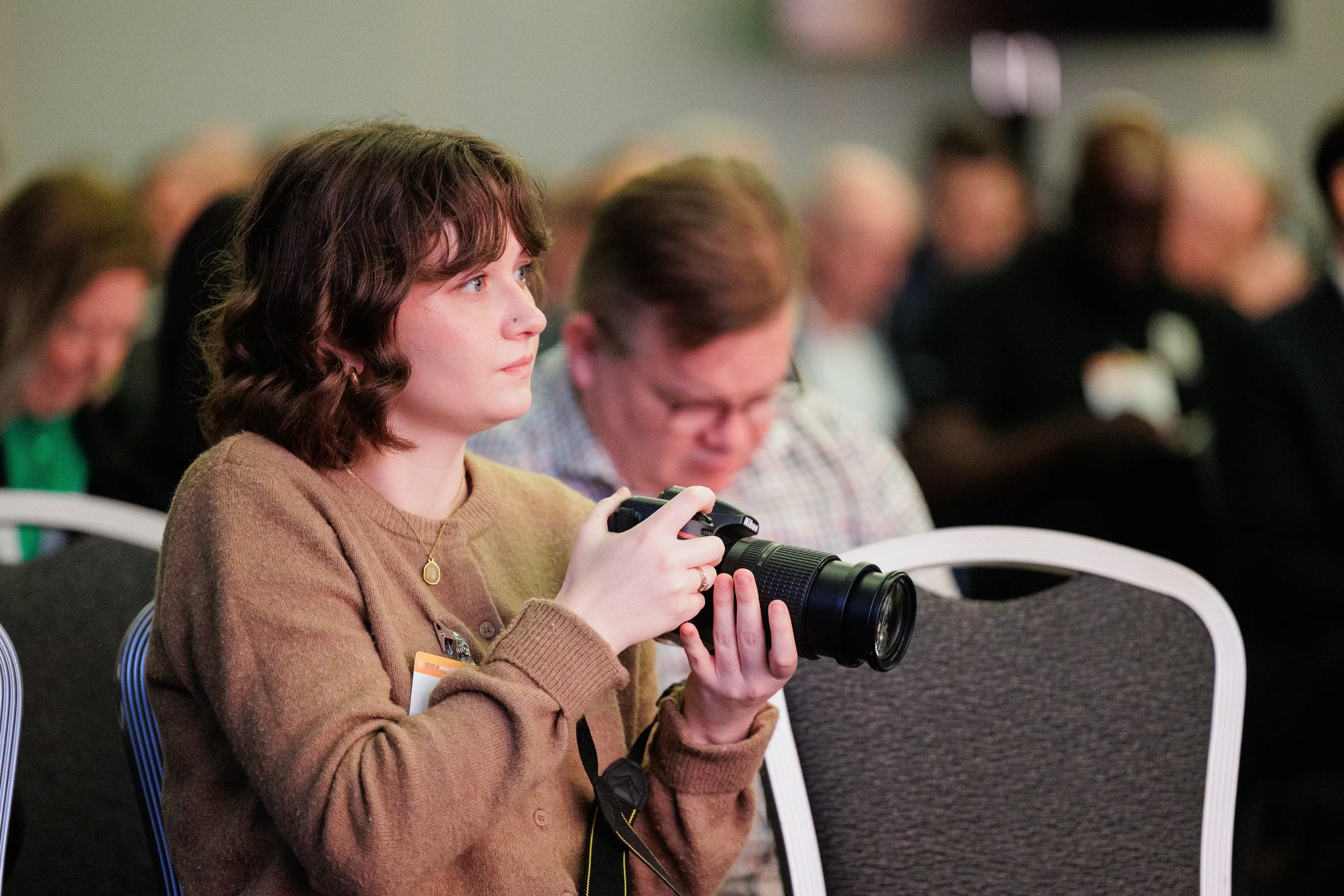 Attendee with name badge holds camera with telephoto lens during session at Orlando industry conference