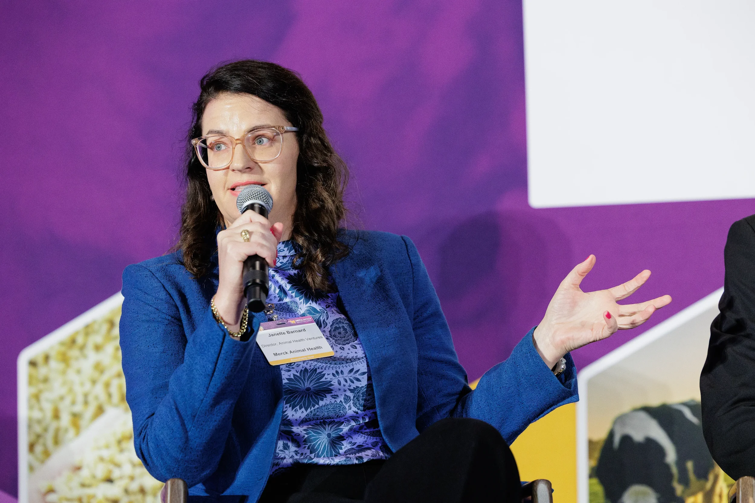 Panelist gestures while speaking into microphone during seated discussion at Orlando industry conference