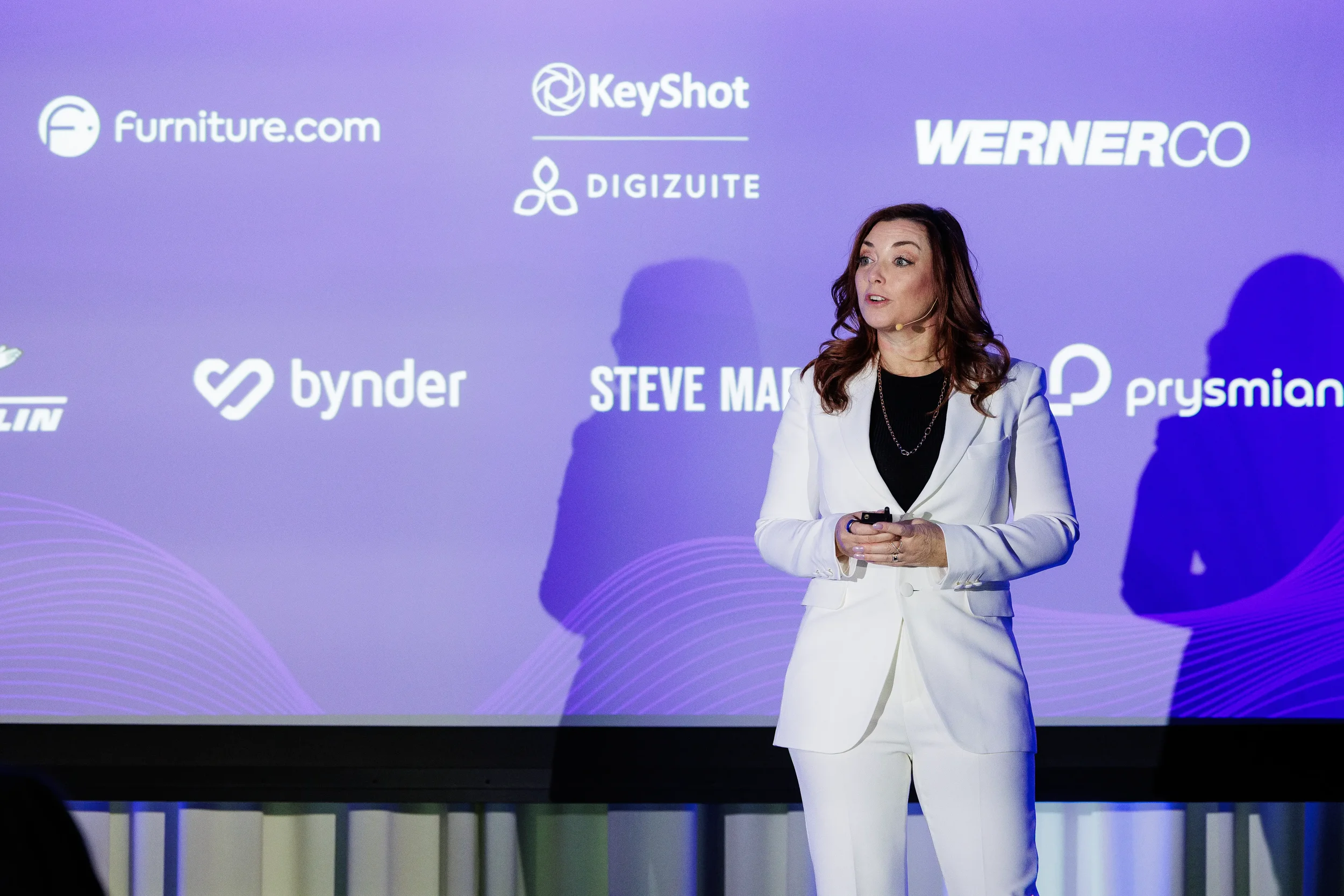Speaker in white suit presents in front of company logo slide on stage at Chicago industry conference