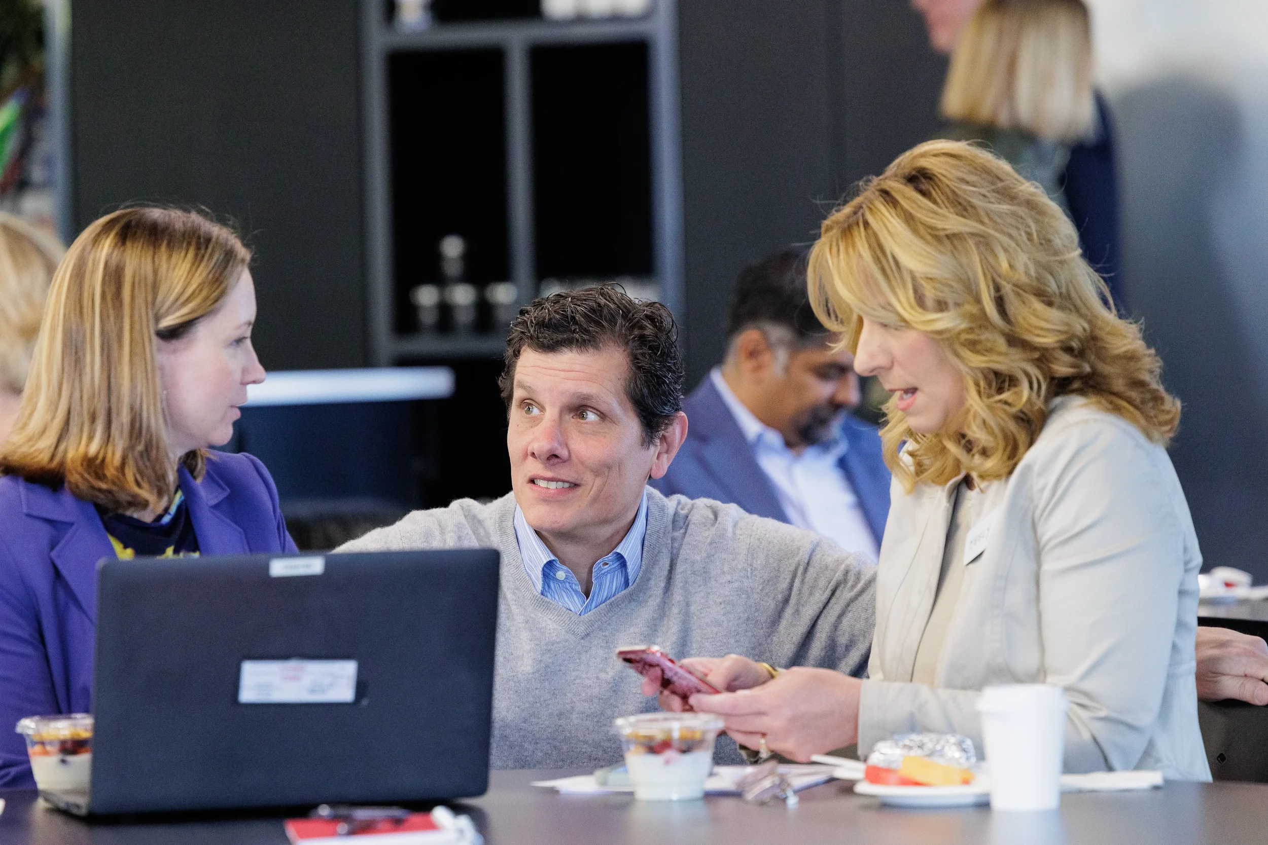 Three attendees converse at a table with a laptop during a session break at Orlando conference