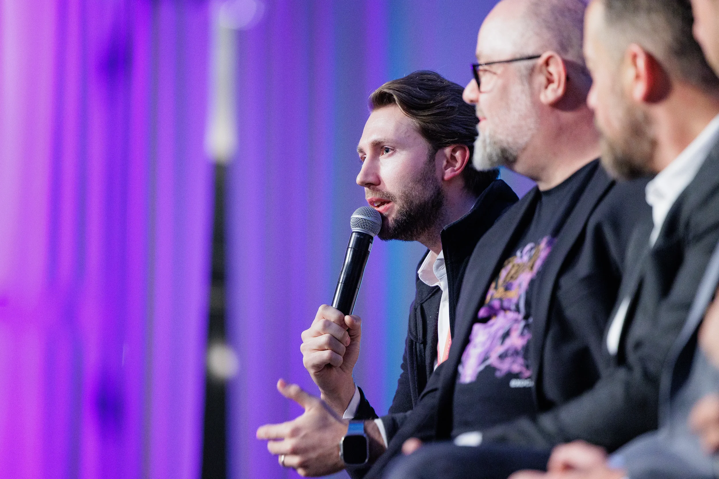 Panelist speaks into microphone in close-up while fellow panelists listen at Orlando industry conference