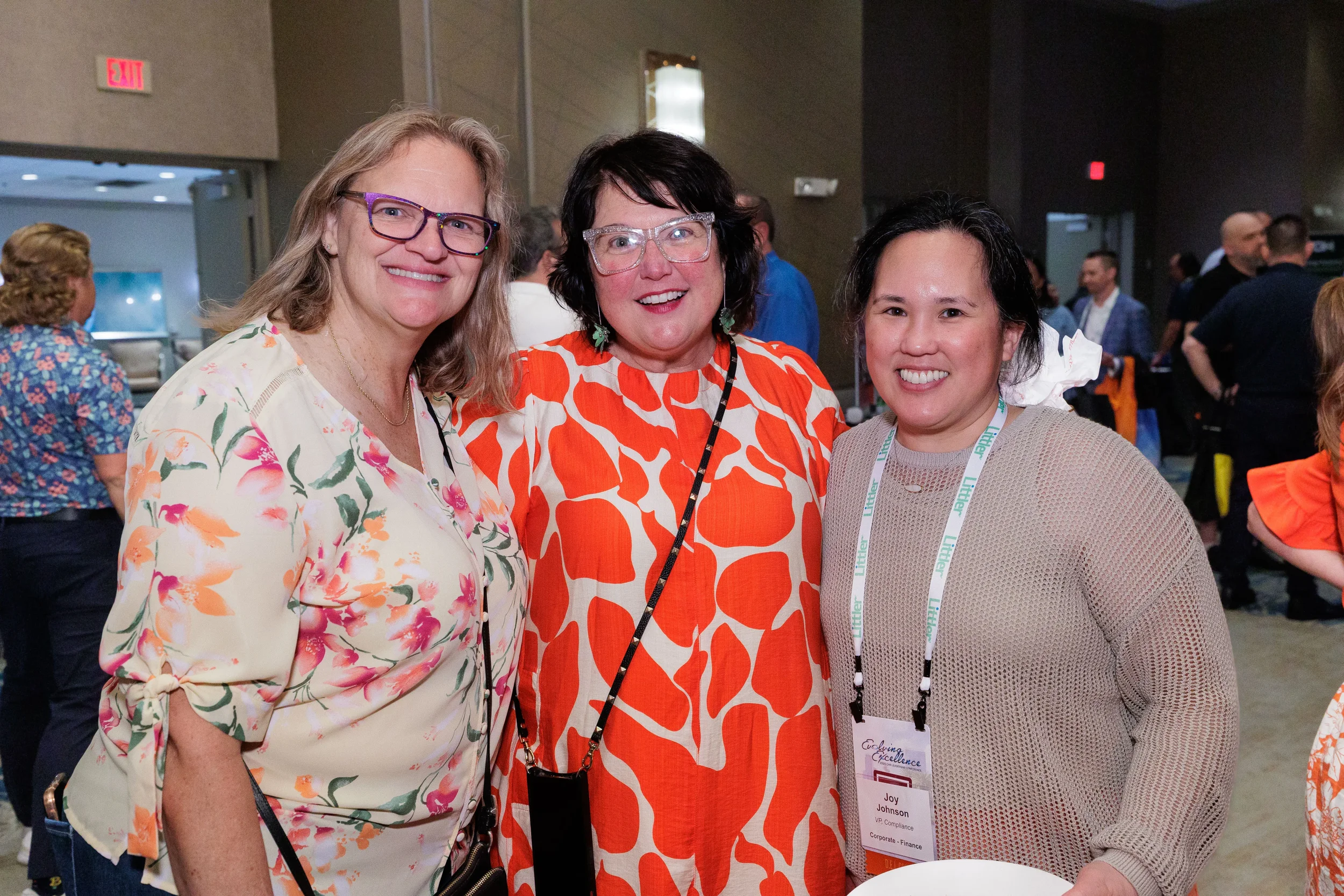Three female attendees with lanyards smile together at Orlando corporate conference networking reception