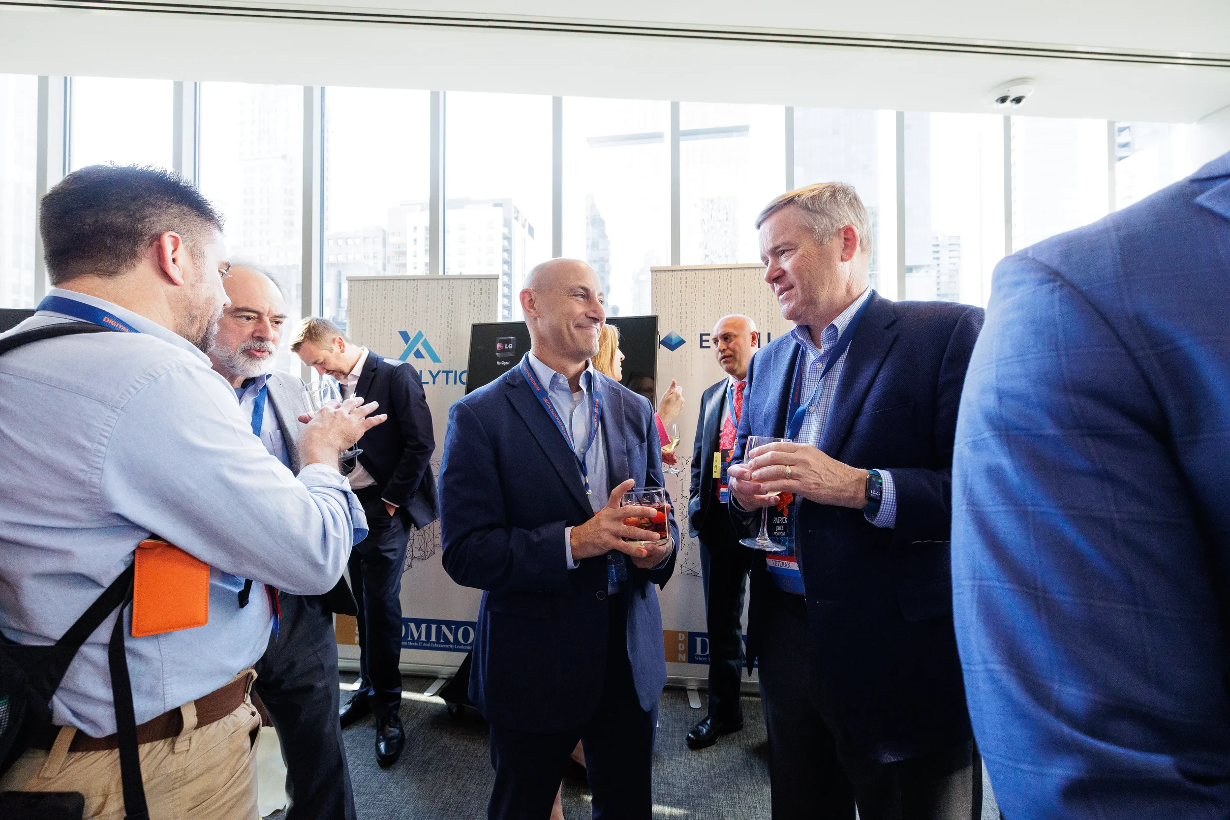 Attendees with lanyards network over drinks near sponsor booths at Chicago corporate event with skyline
