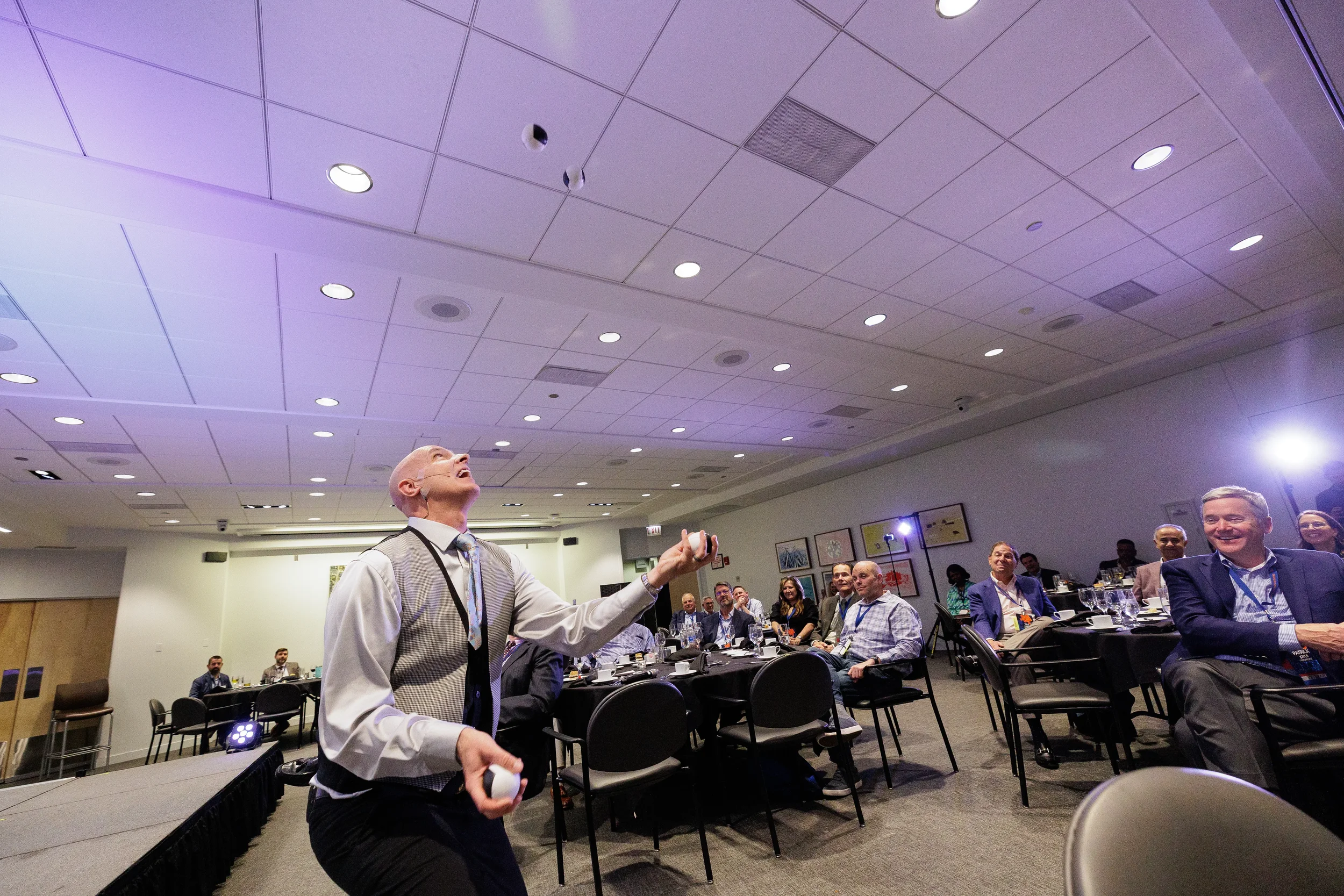 Entertainer tosses juggling balls on stage before laughing audience at Orlando corporate conference event