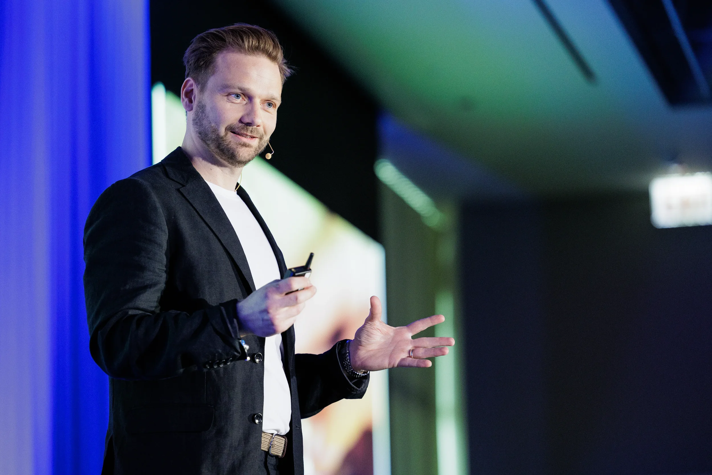 Smiling speaker with headset microphone gestures while holding clicker on stage at Orlando corporate event