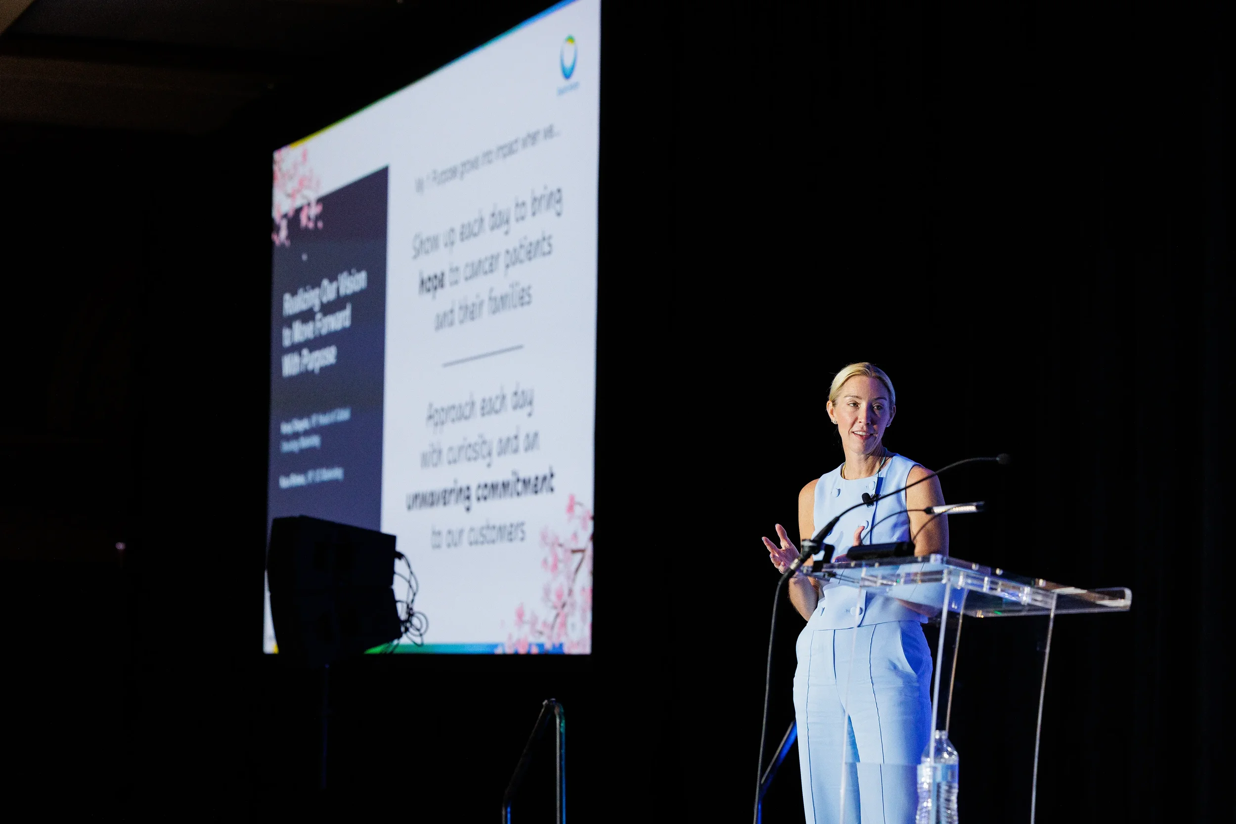 Speaker gestures while presenting from podium with presentation screen at Chicago corporate event