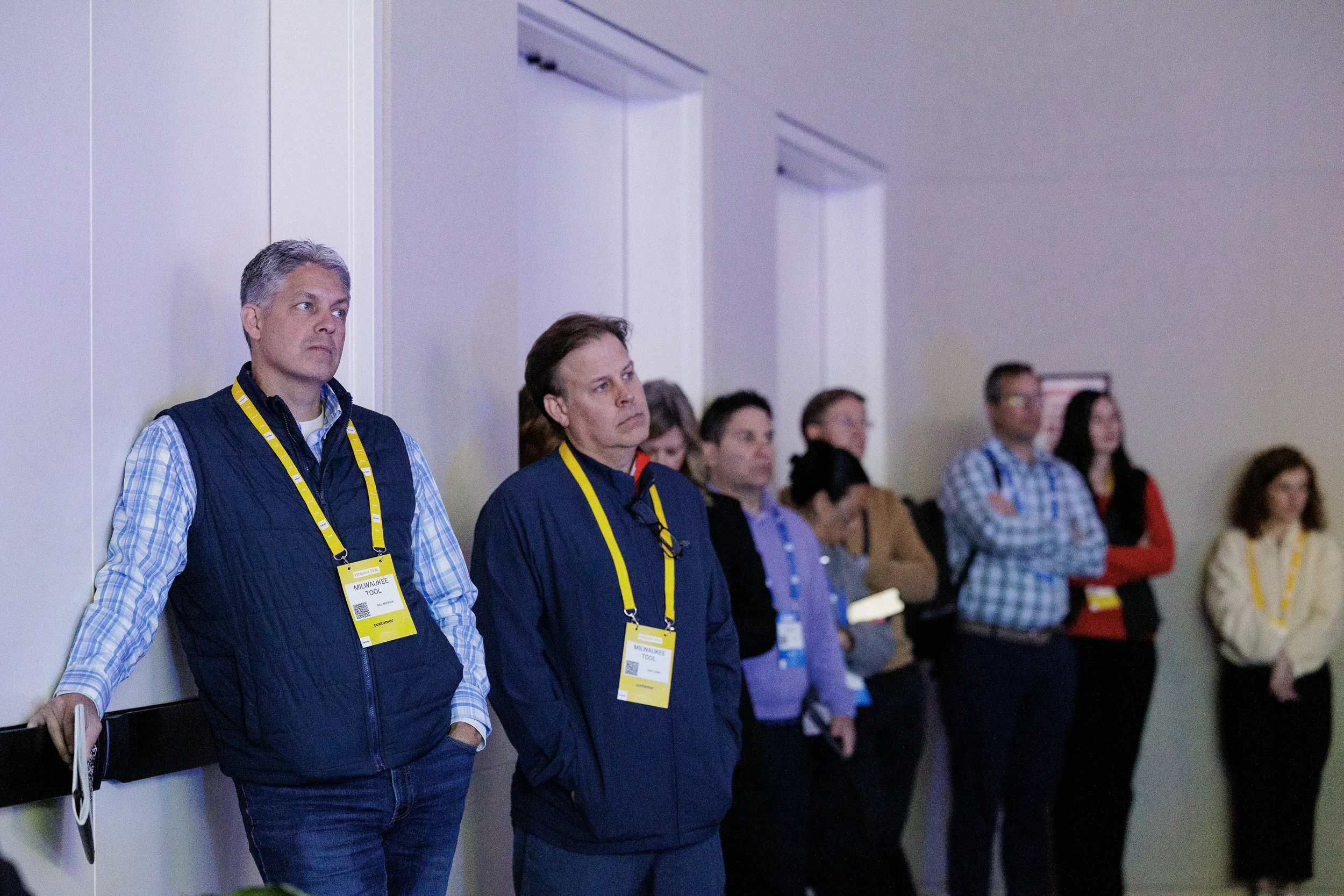 Attendees with yellow lanyards stand along wall watching session at Chicago corporate conference