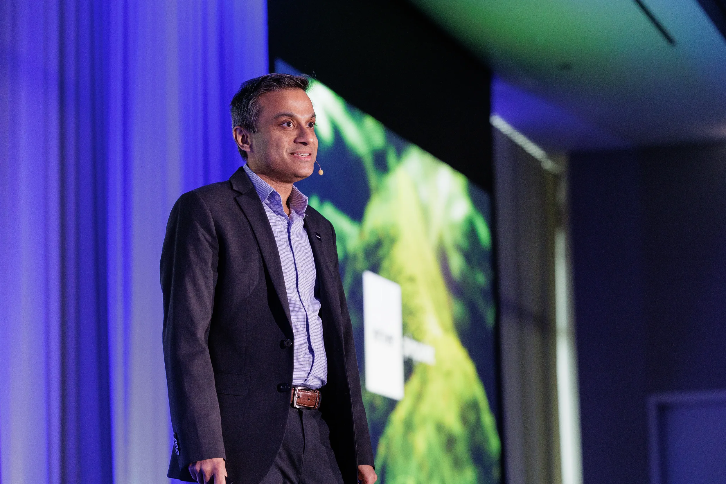 Speaker in dark blazer with headset microphone presents beside projection screen at Orlando conference