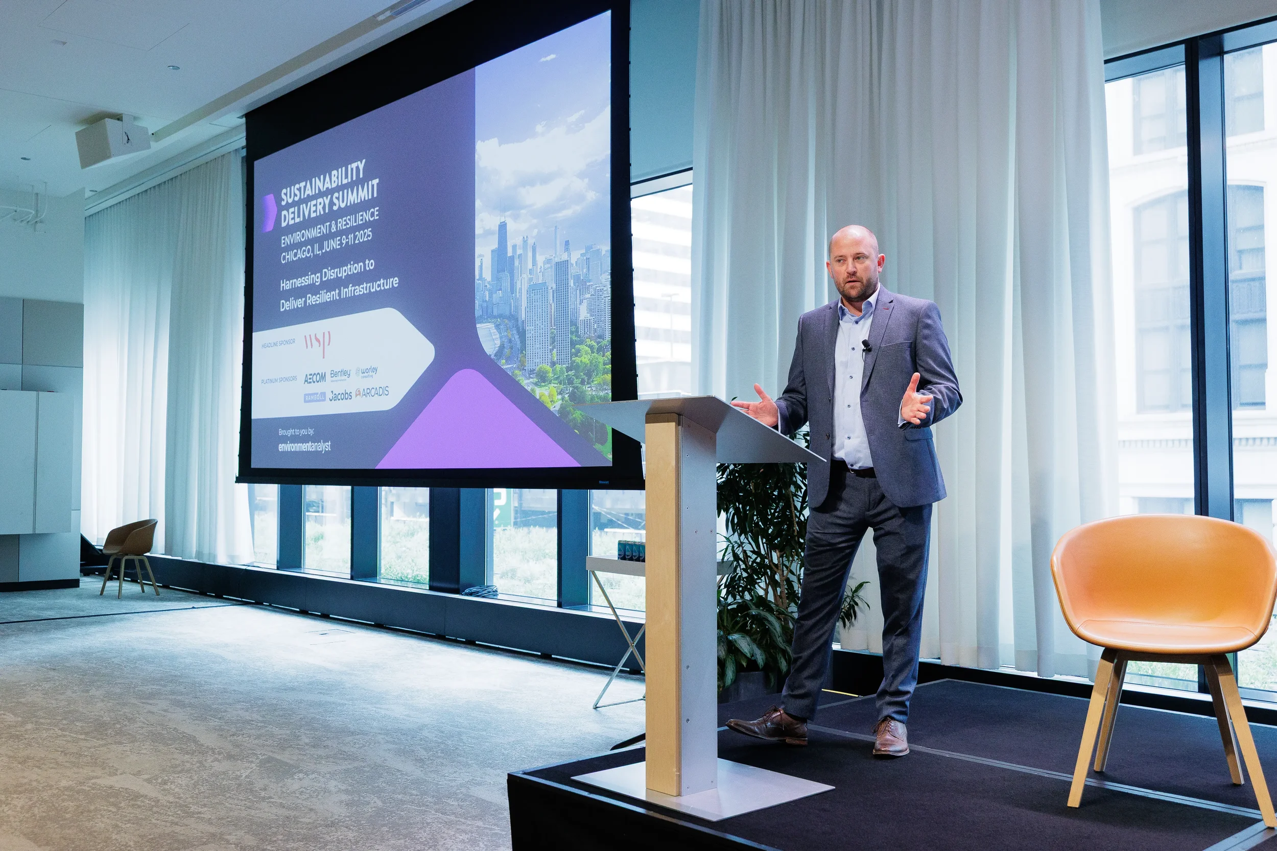 Speaker gestures from podium during presentation with screen behind at Chicago industry summit
