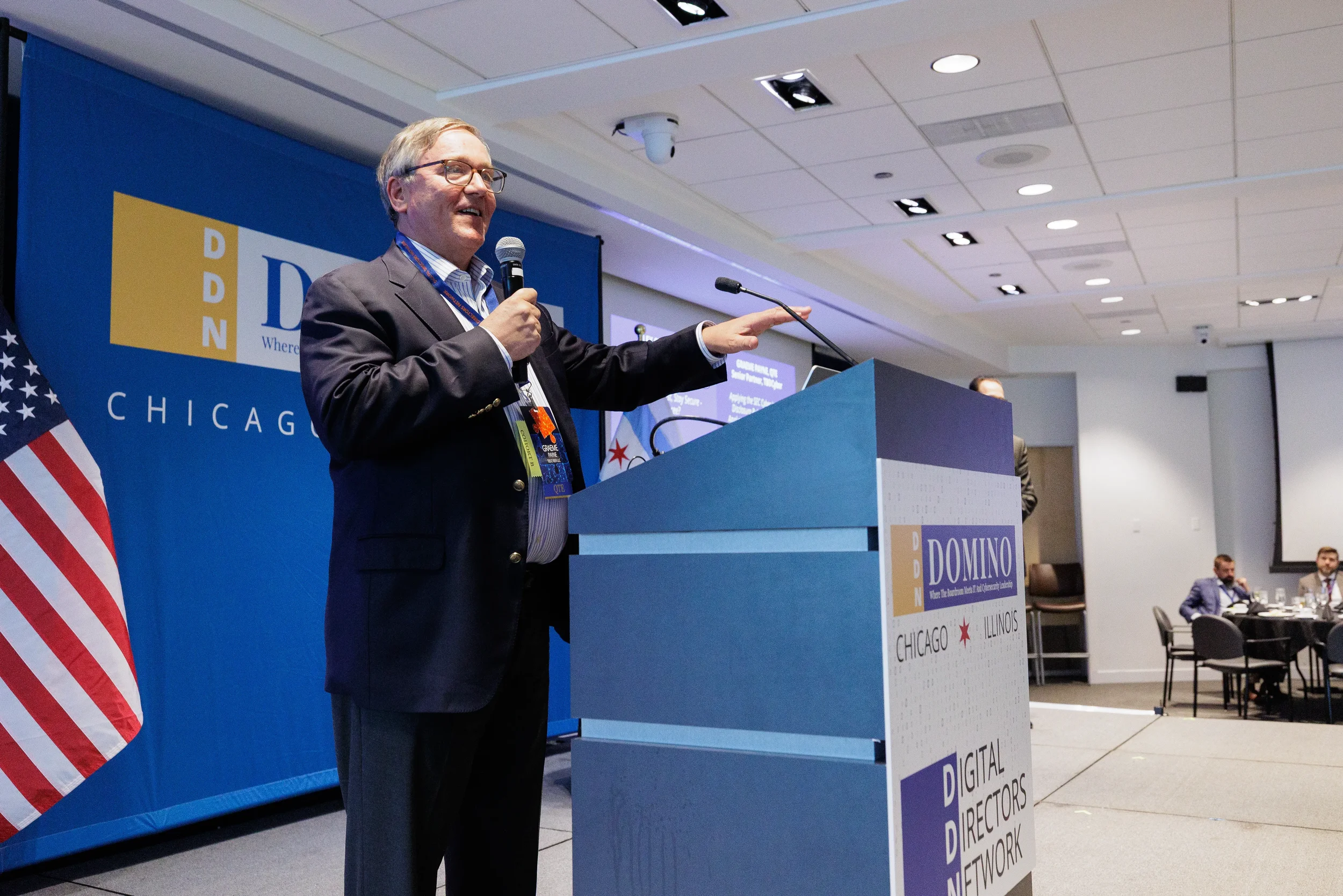 Male speaker holds microphone and points from branded podium at Chicago corporate conference event