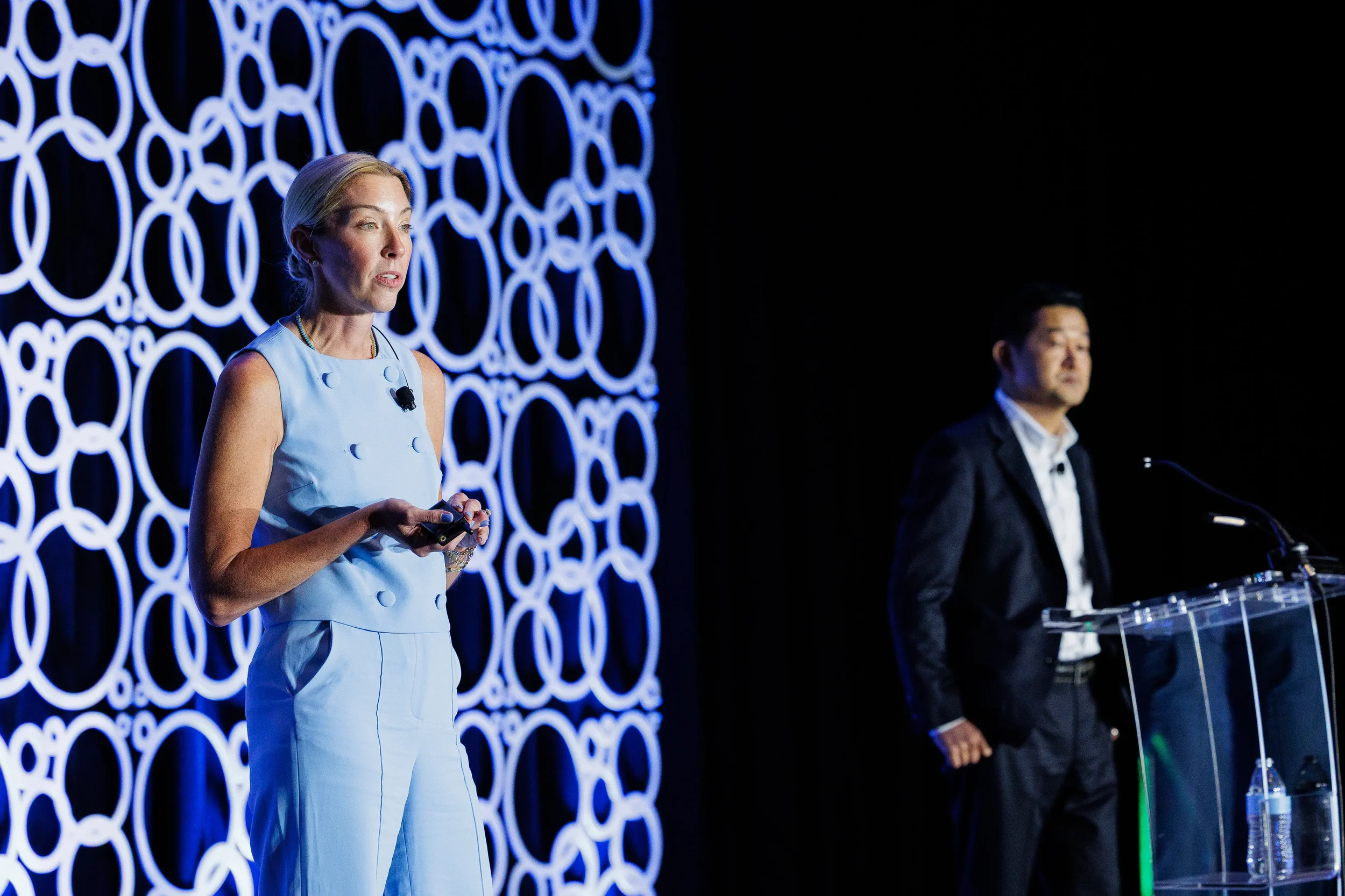 Two speakers present on stage with illuminated circular backdrop at Orlando corporate conference