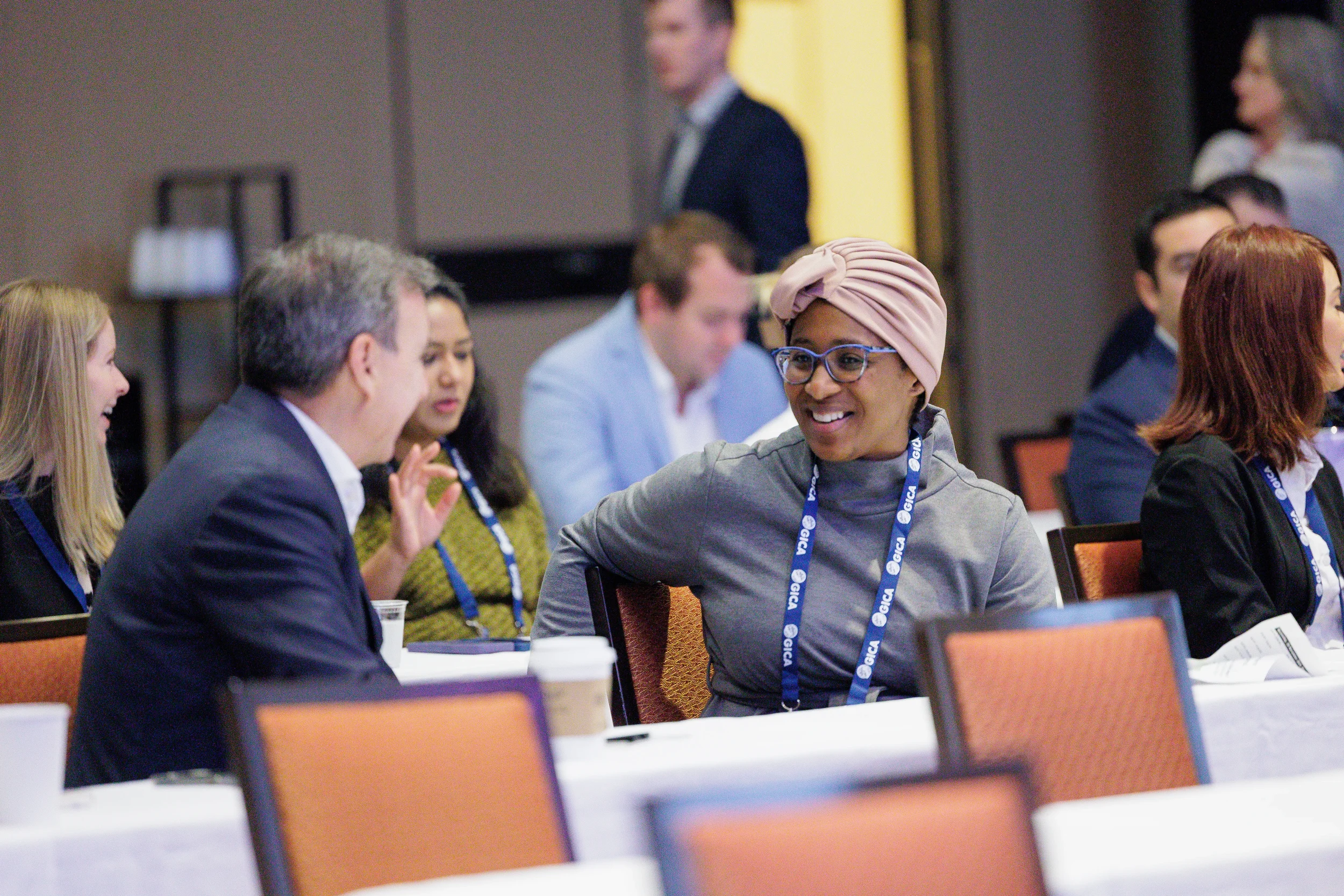 A diverse group of professionals wearing conference lanyards engage in conversation around tables at a meeting in Chicago