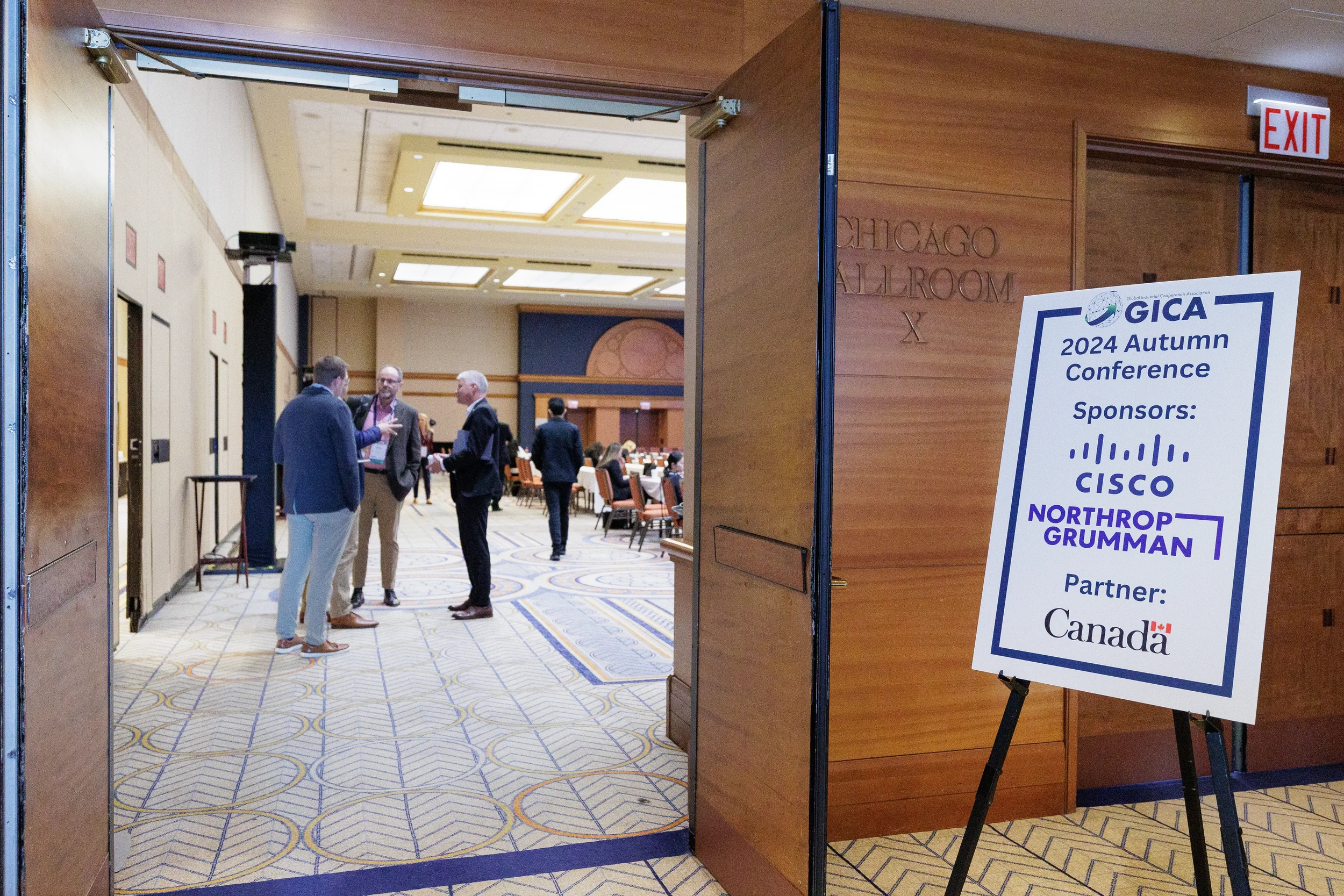 Attendees network in ballroom doorway beside conference sponsor signage at Chicago corporate event