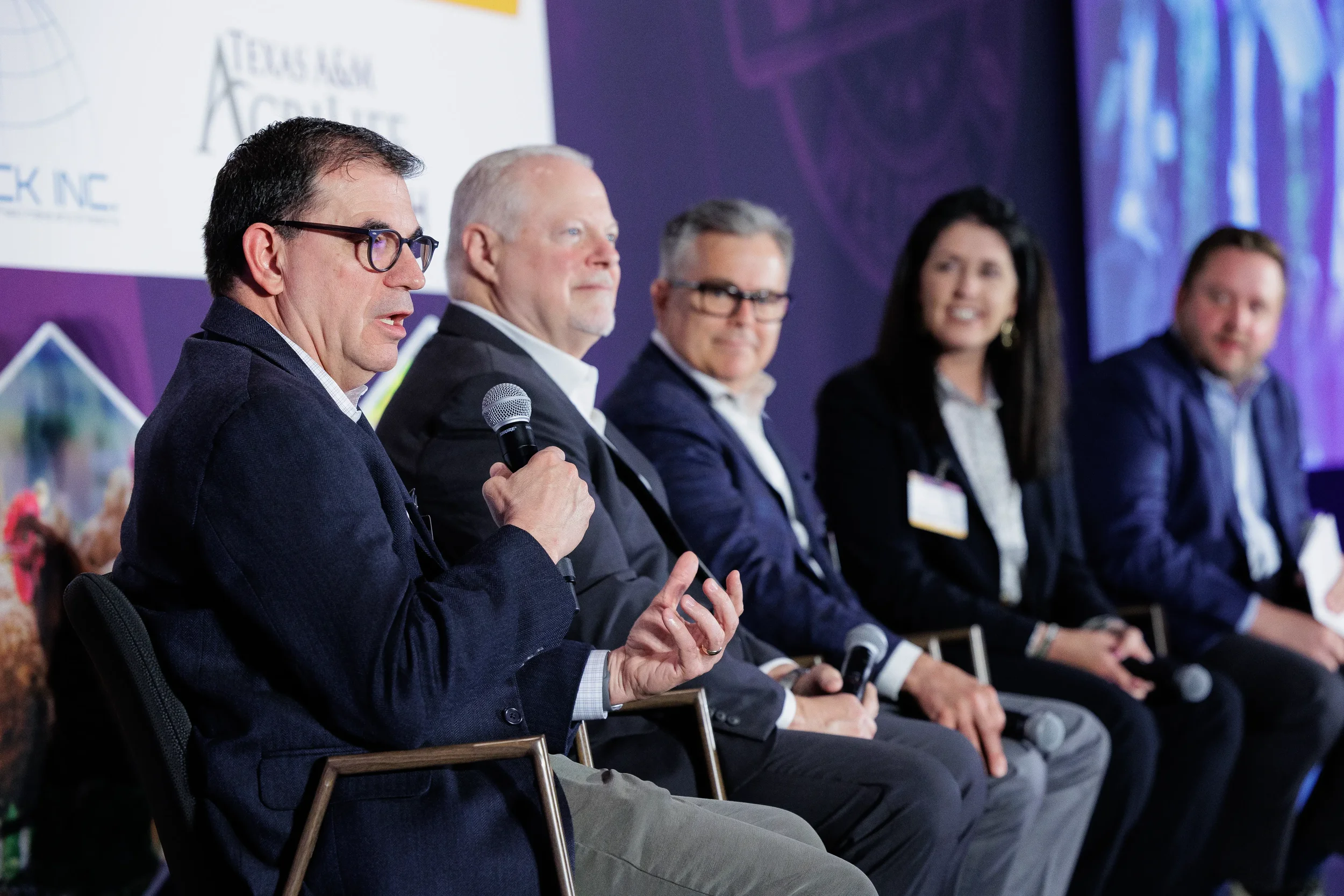 Panelist gestures while speaking into microphone during seated discussion at Chicago summit