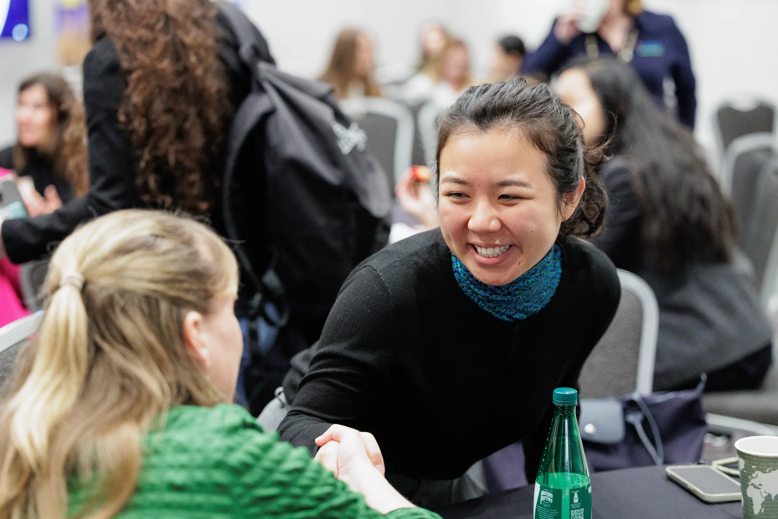 Two female attendees smile and shake hands across table during networking at Chicago corporate conference