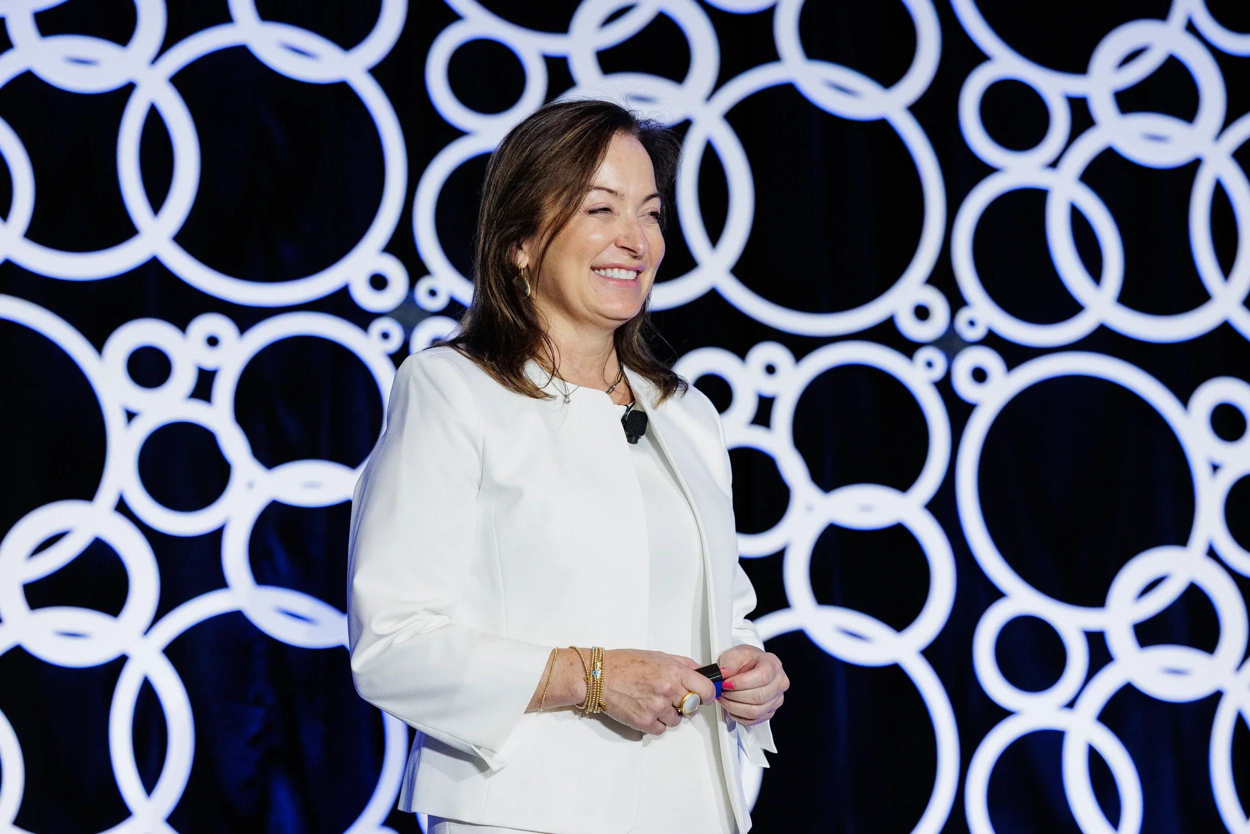 Presenter in white suit smiles on stage with circle-patterned backdrop at Chicago industry conference