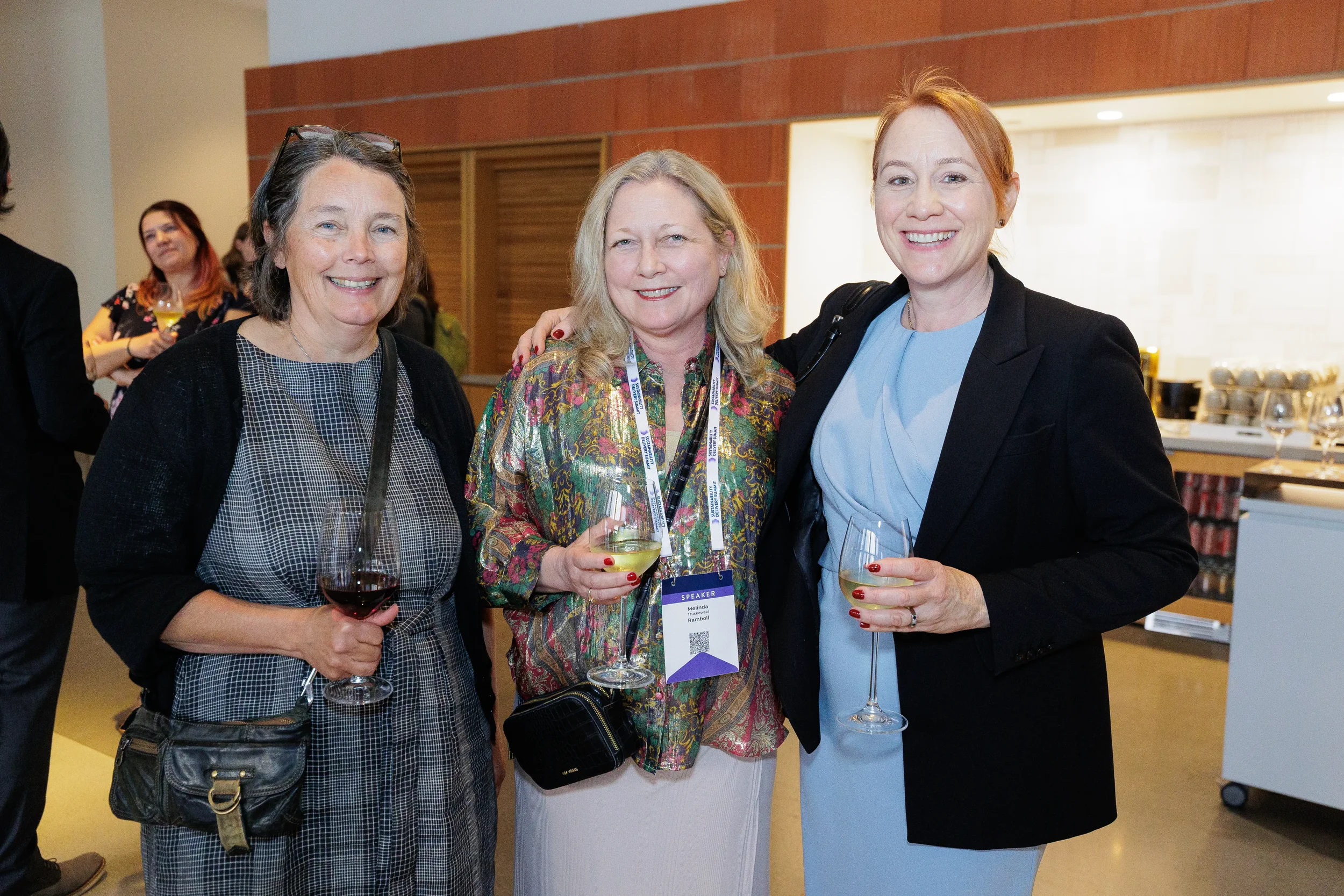 Three attendees smile together holding wine glasses at Chicago corporate event reception