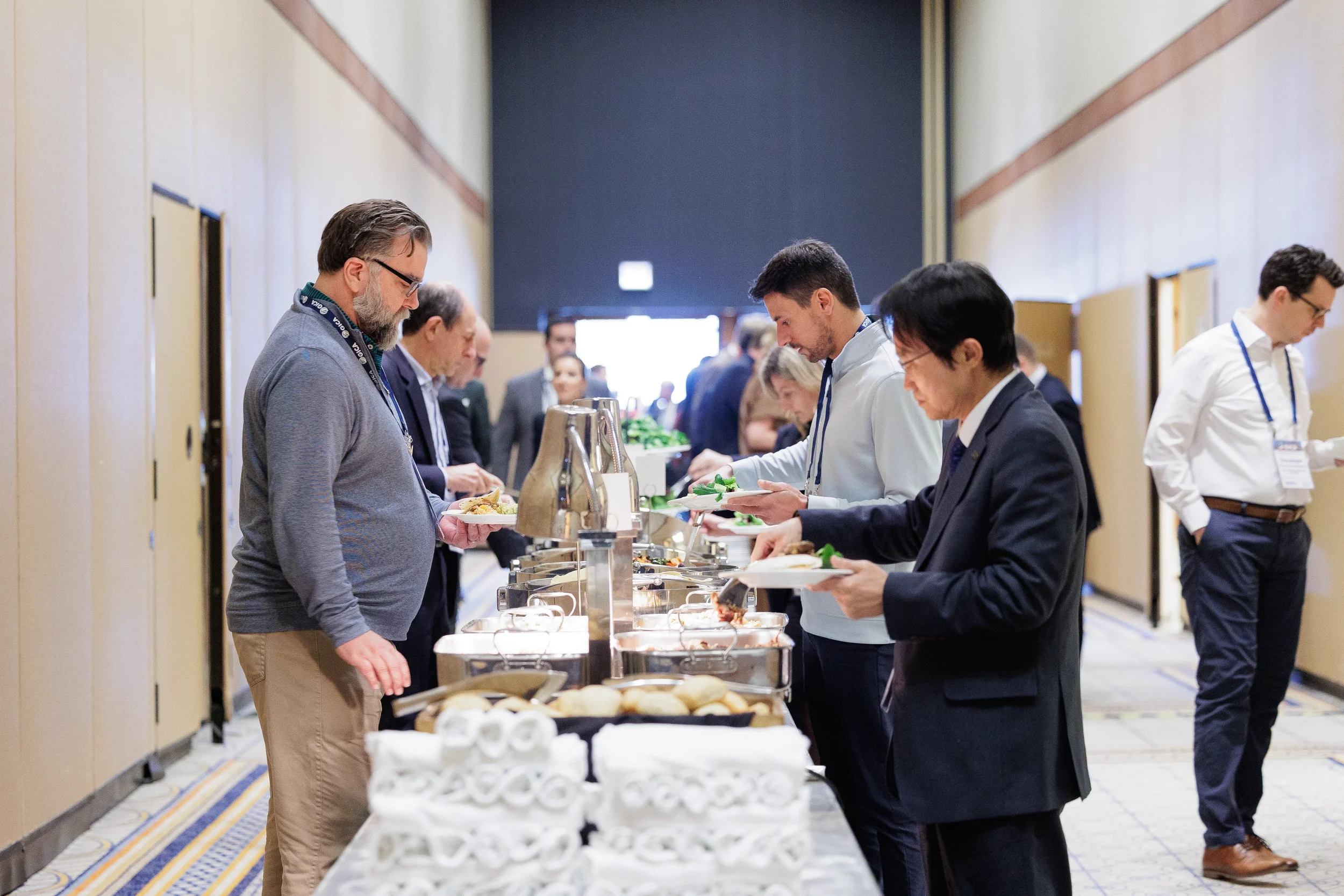Business professionals at a conference in Orlando line up in hallway to serve themselves food from a long buffet table