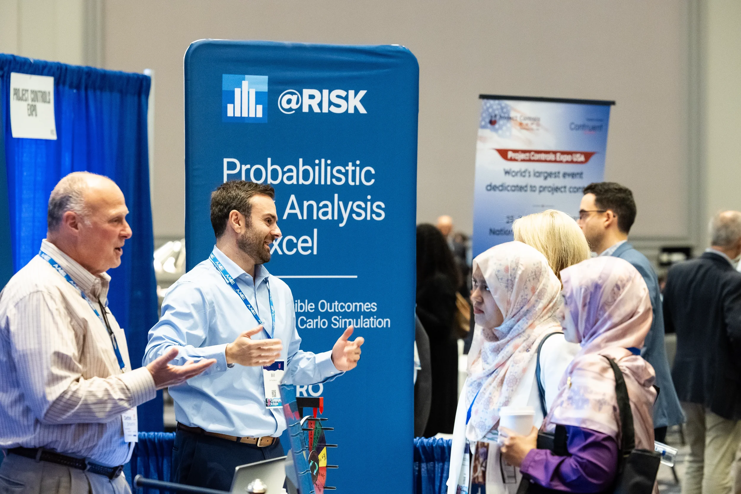 Exhibitor gestures while speaking with attendees at trade show booth on expo floor at Orlando industry conference