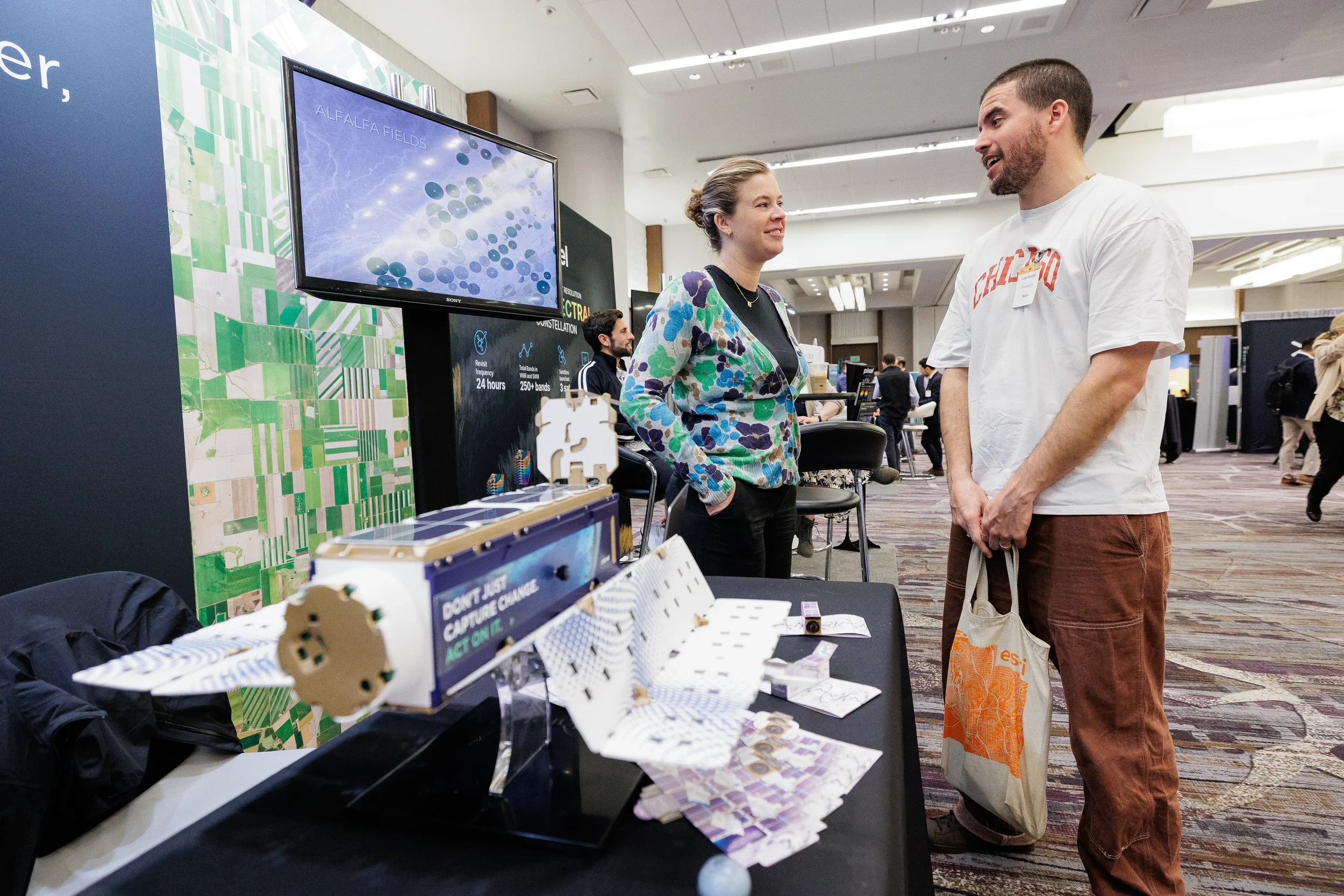 Two attendees view satellite technology display at exhibitor booth on Chicago industry conference expo floor