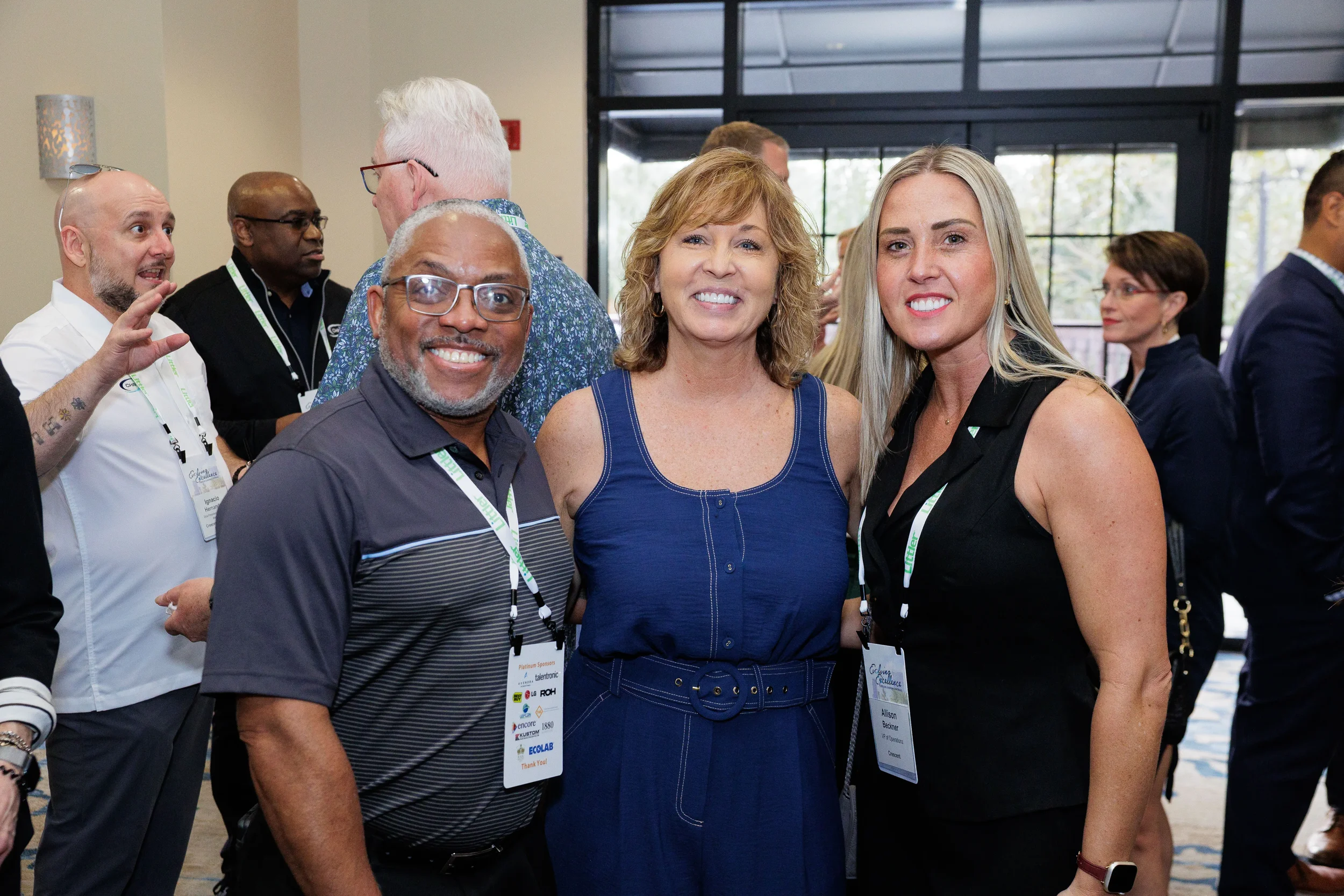Three attendees with lanyards smile together during outdoor networking reception at Orlando industry conference