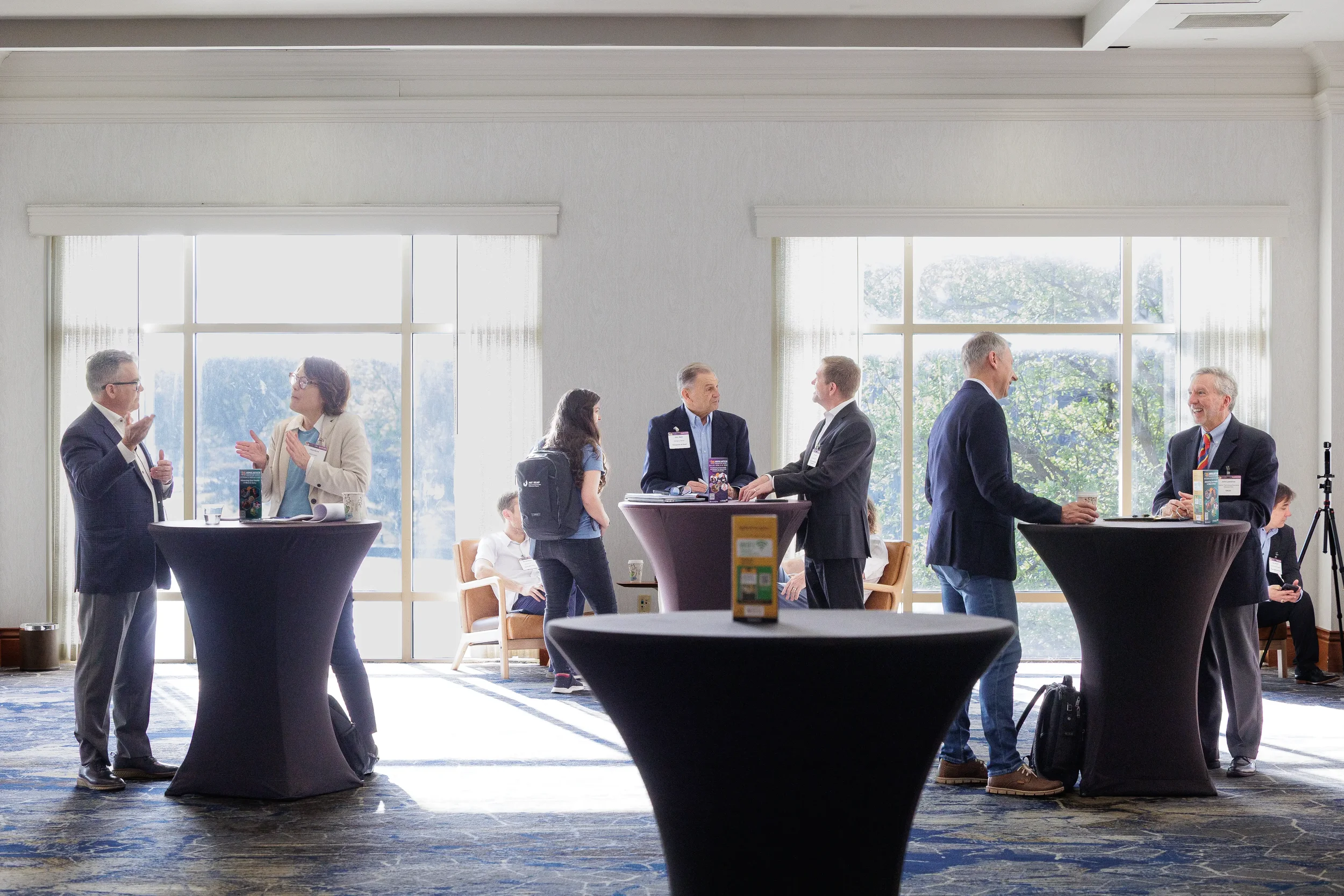 Attendees network at standing tables in sunlit lobby at Orlando corporate conference