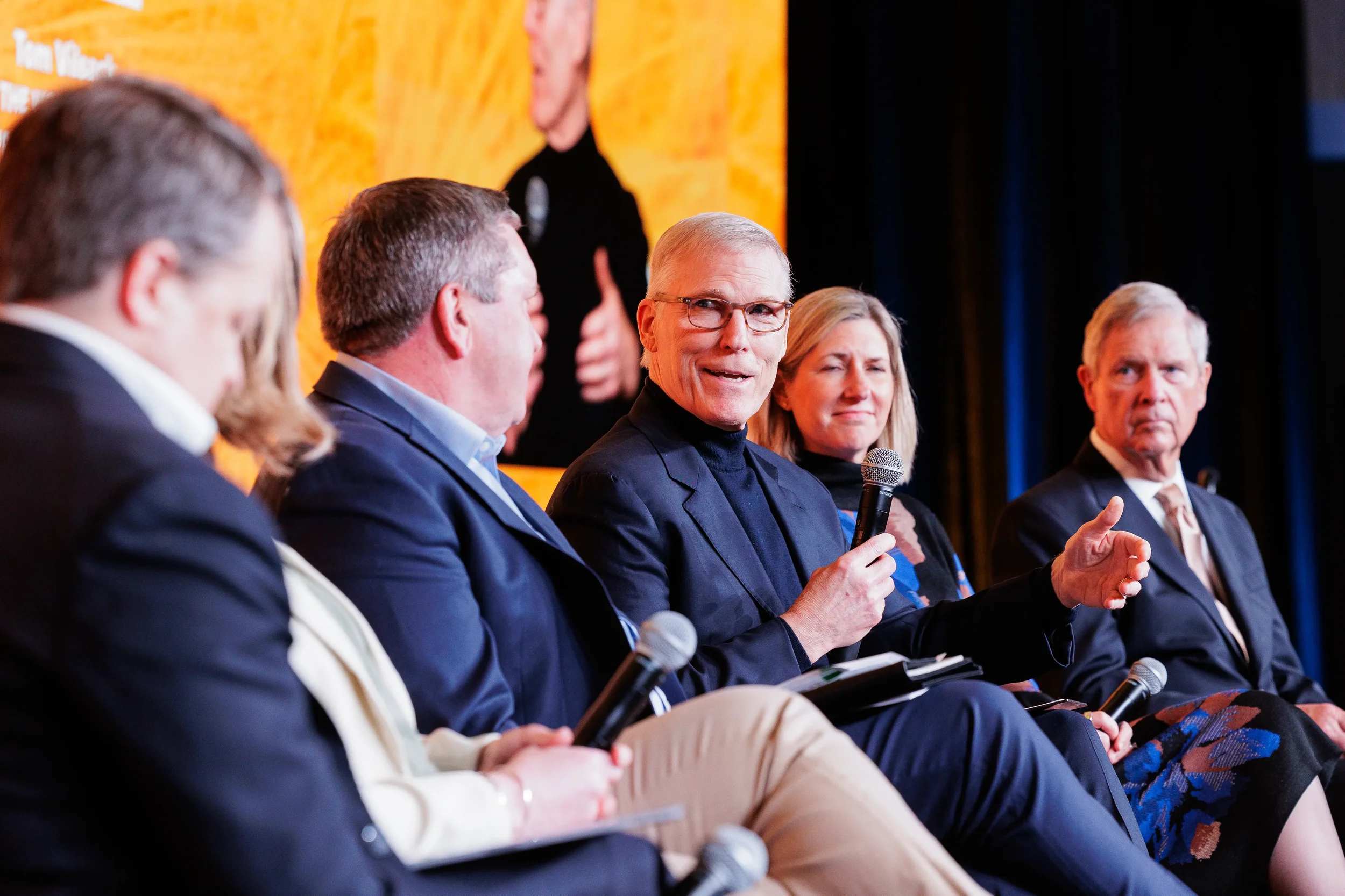 Male panelist in turtleneck speaks into microphone and gestures to fellow panelists at Orlando industry conference