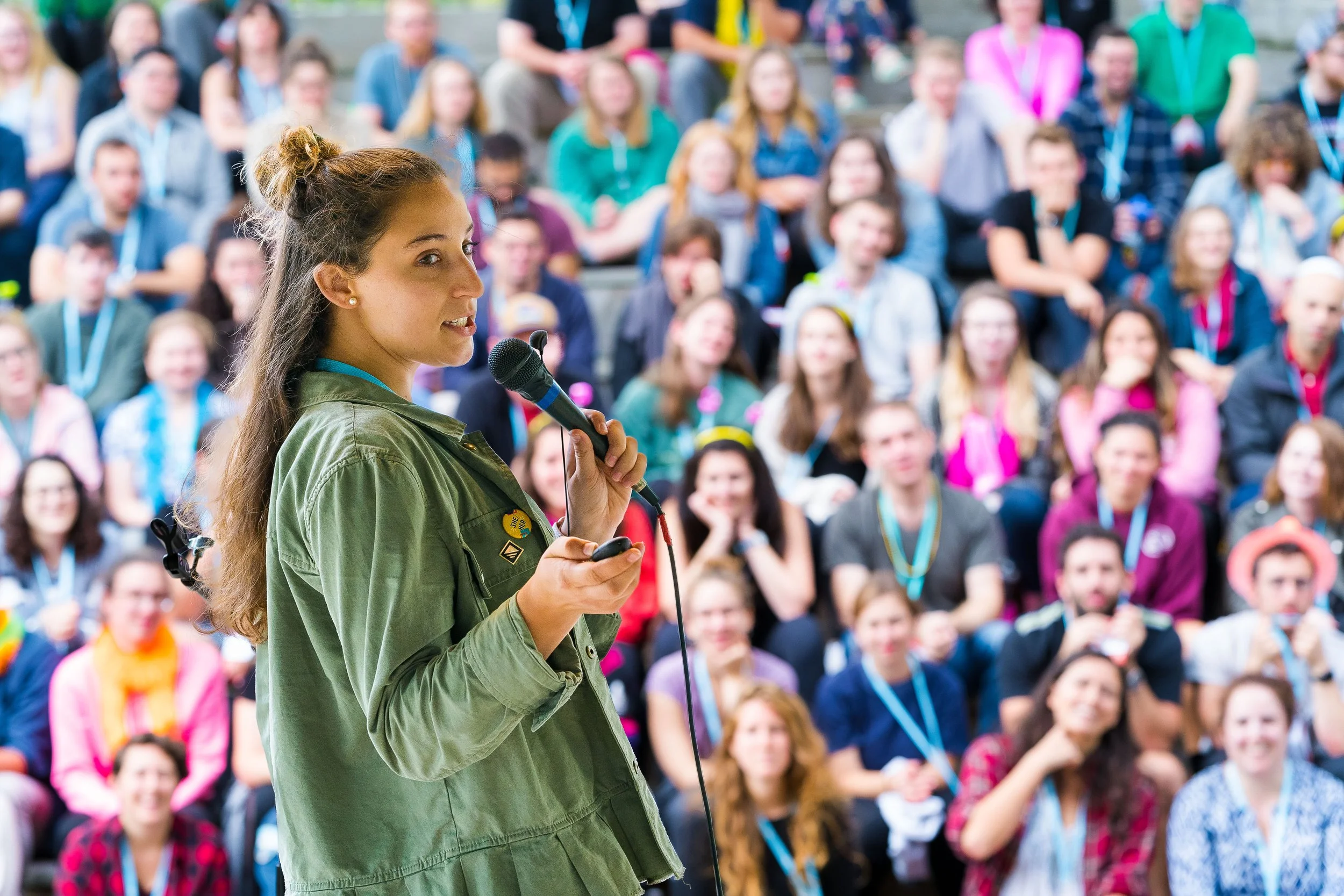 Speaker addressing large crowd of engaged attendees from amphitheater stage at outdoor conference event in Chicago