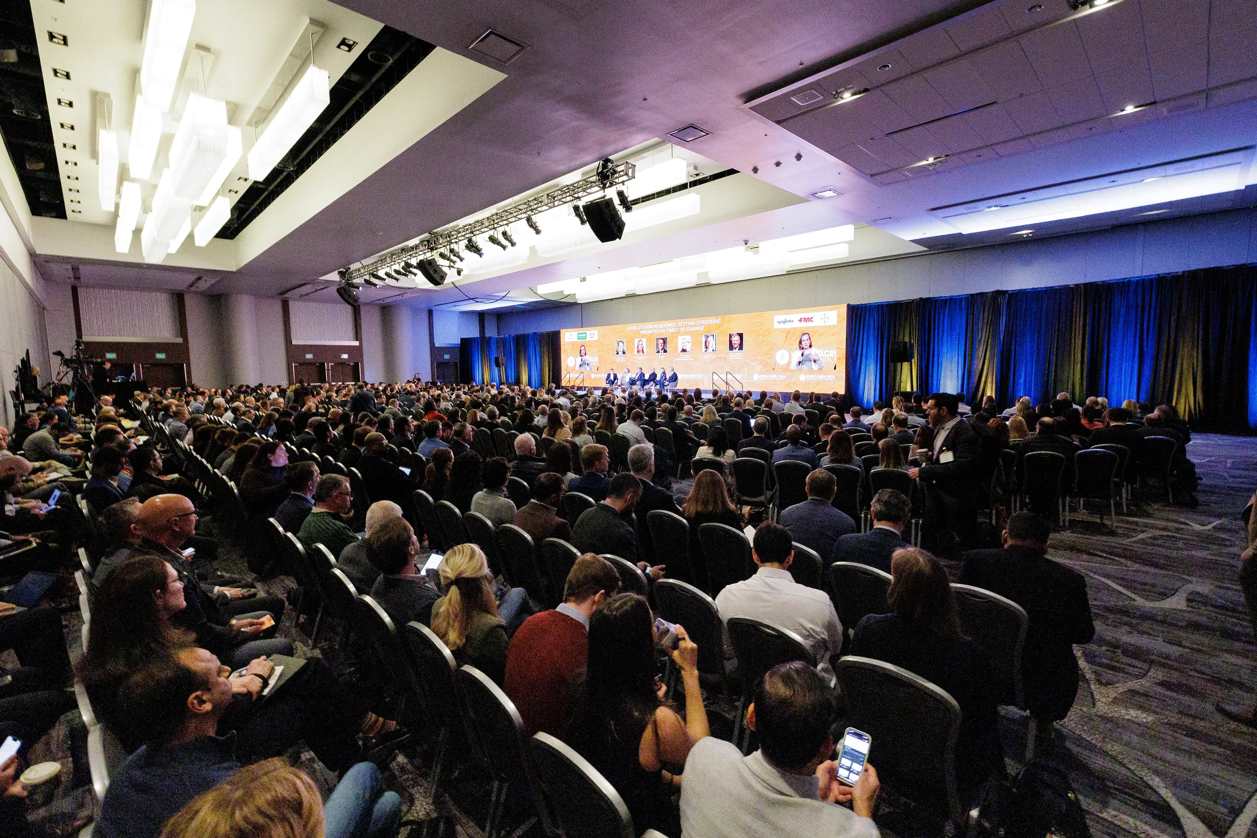 Wide shot of packed ballroom audience facing panel on branded stage at Chicago industry conference